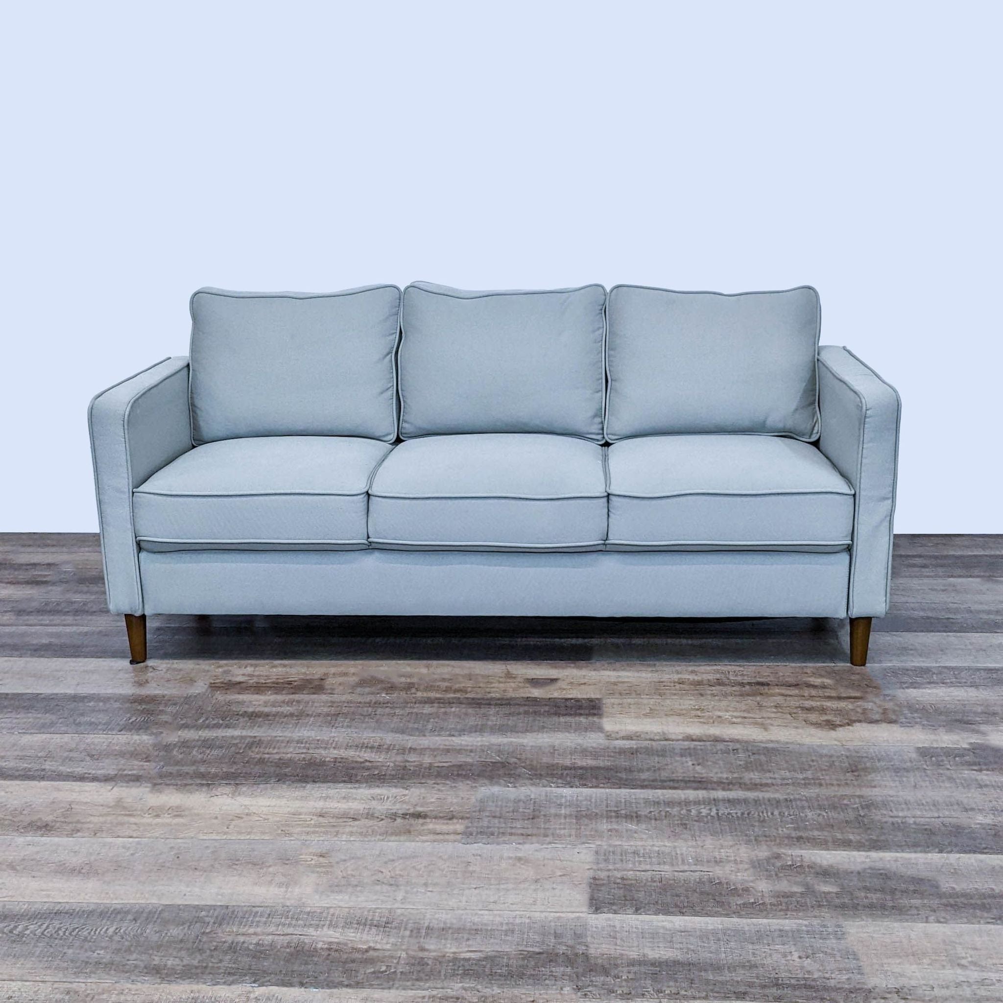 Reperch brand 3-seat sofa with gray upholstery and narrow wooden legs, against a wooden floor background.