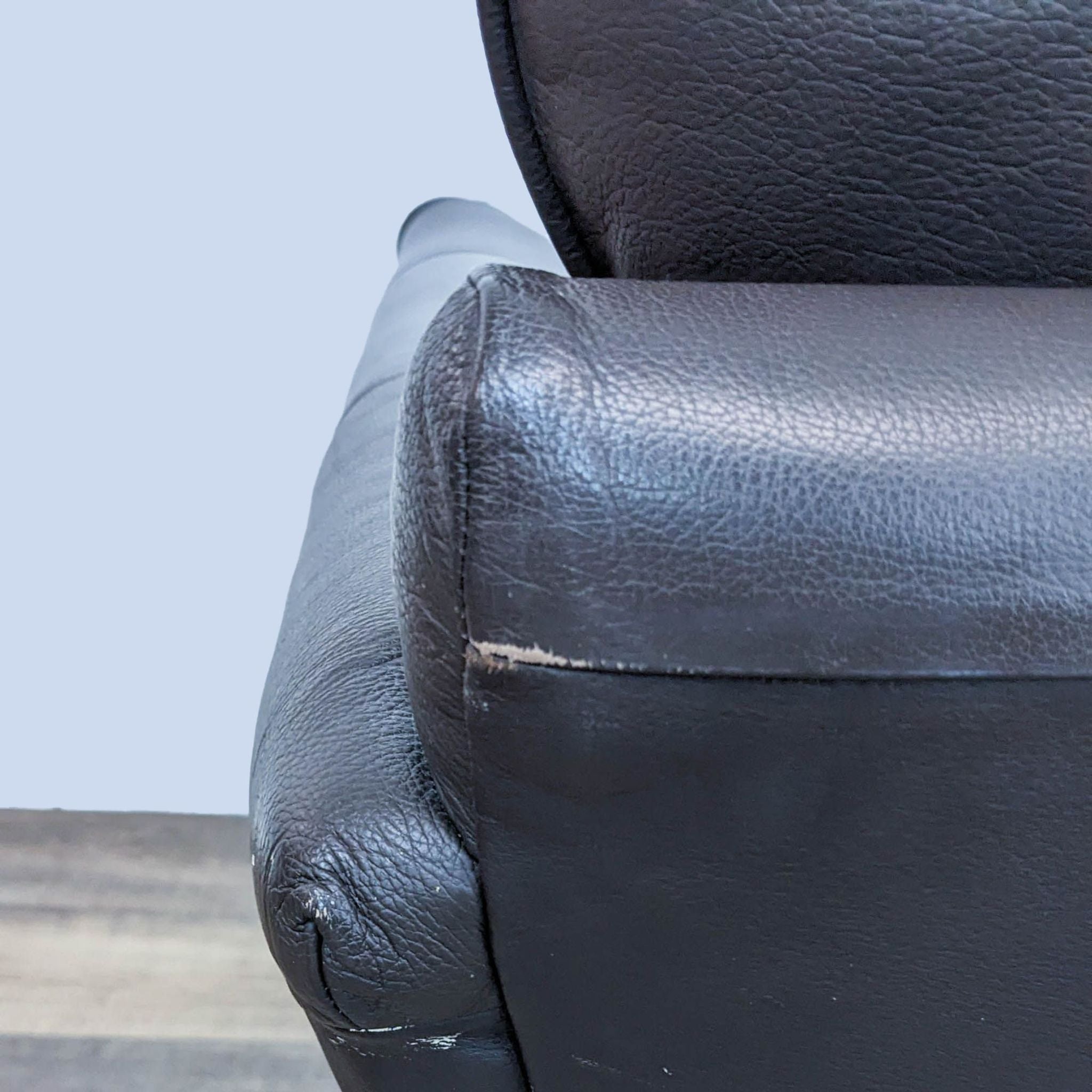 Close-up of a black Marks & Spencer leather lounge chair arm with visible wear and wooden feet.