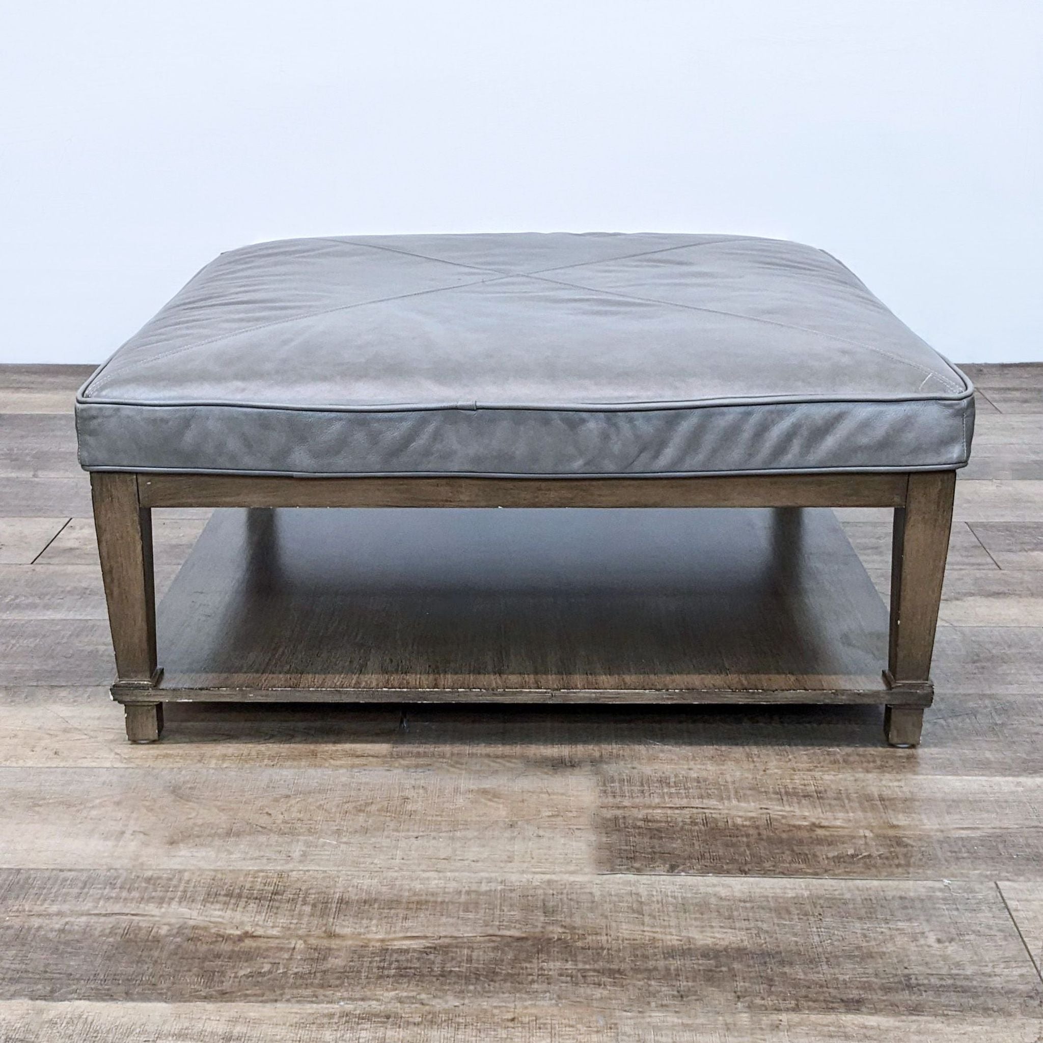 Bassett 40" square gray leather ottoman with wooden frame and lower shelf.