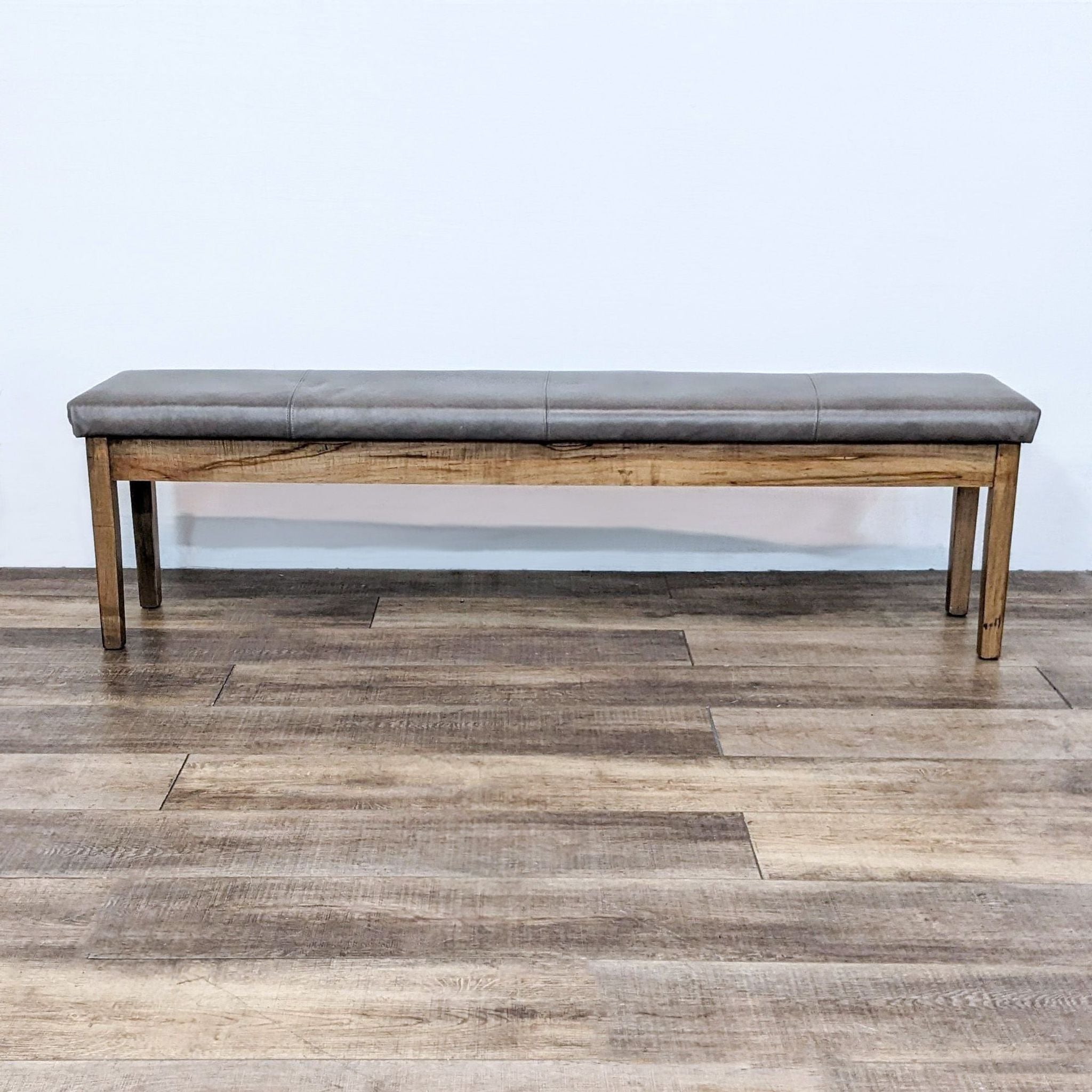 Alt text 1: Bassett 70" wooden bench with a gray padded leather look seat, displayed in a room with wood-patterned flooring.