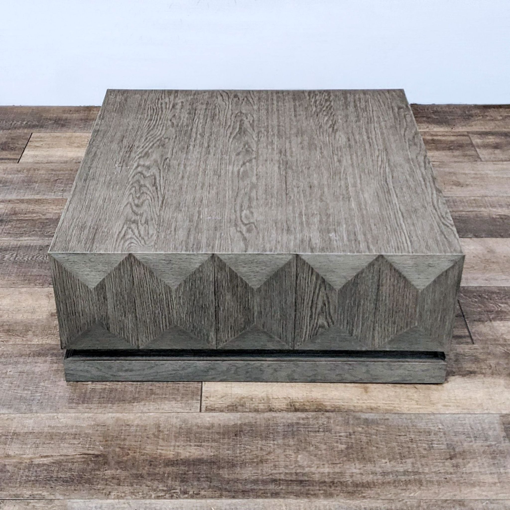 Modern Reperch gray coffee table in block design, showcasing angular detailing, set on patterned flooring.