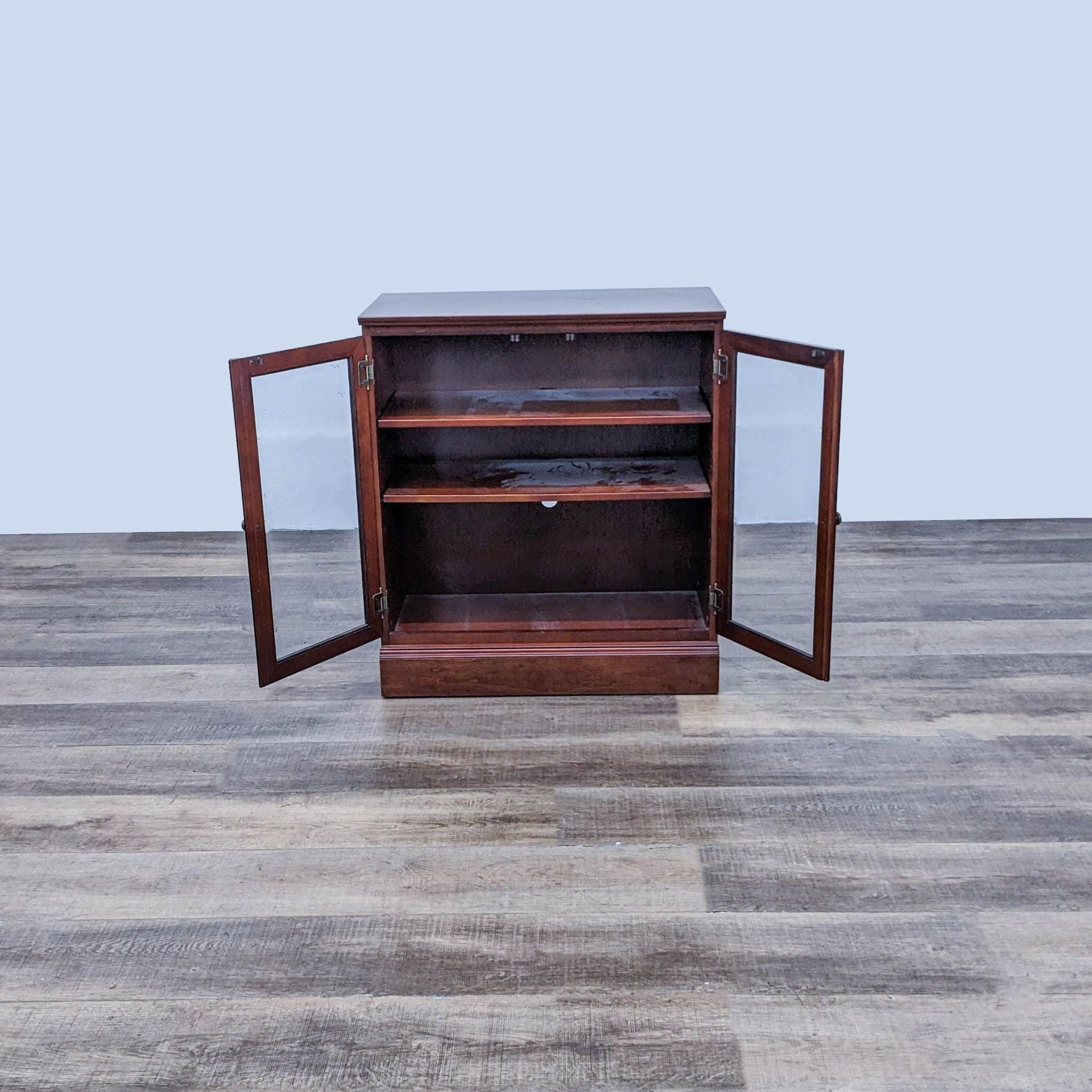Bombay Company wooden bookcase open showing adjustable shelves, on a wood-patterned floor against a simple backdrop.