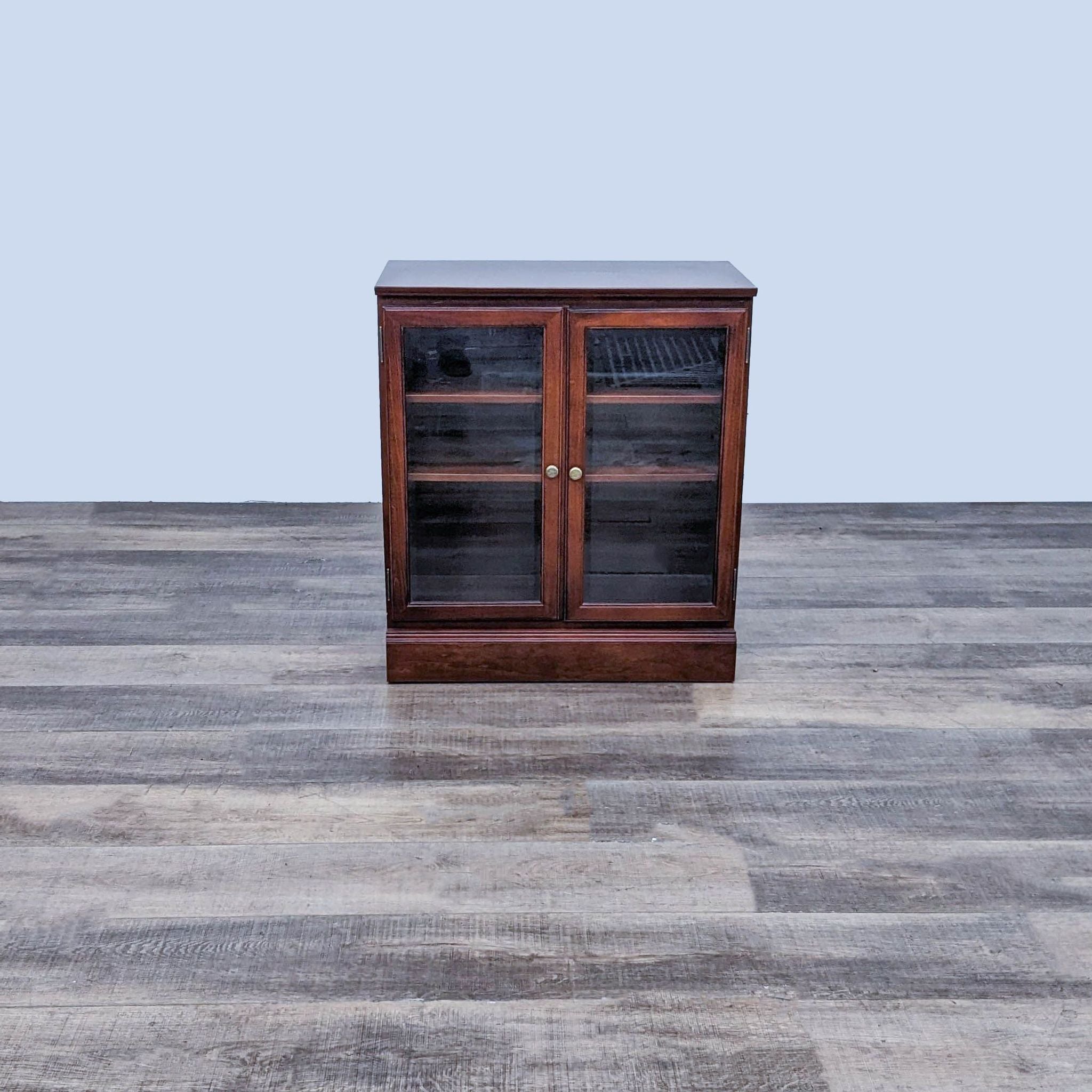 Bombay Company small wooden bookshelf with glass doors and adjustable shelves on a wooden floor.