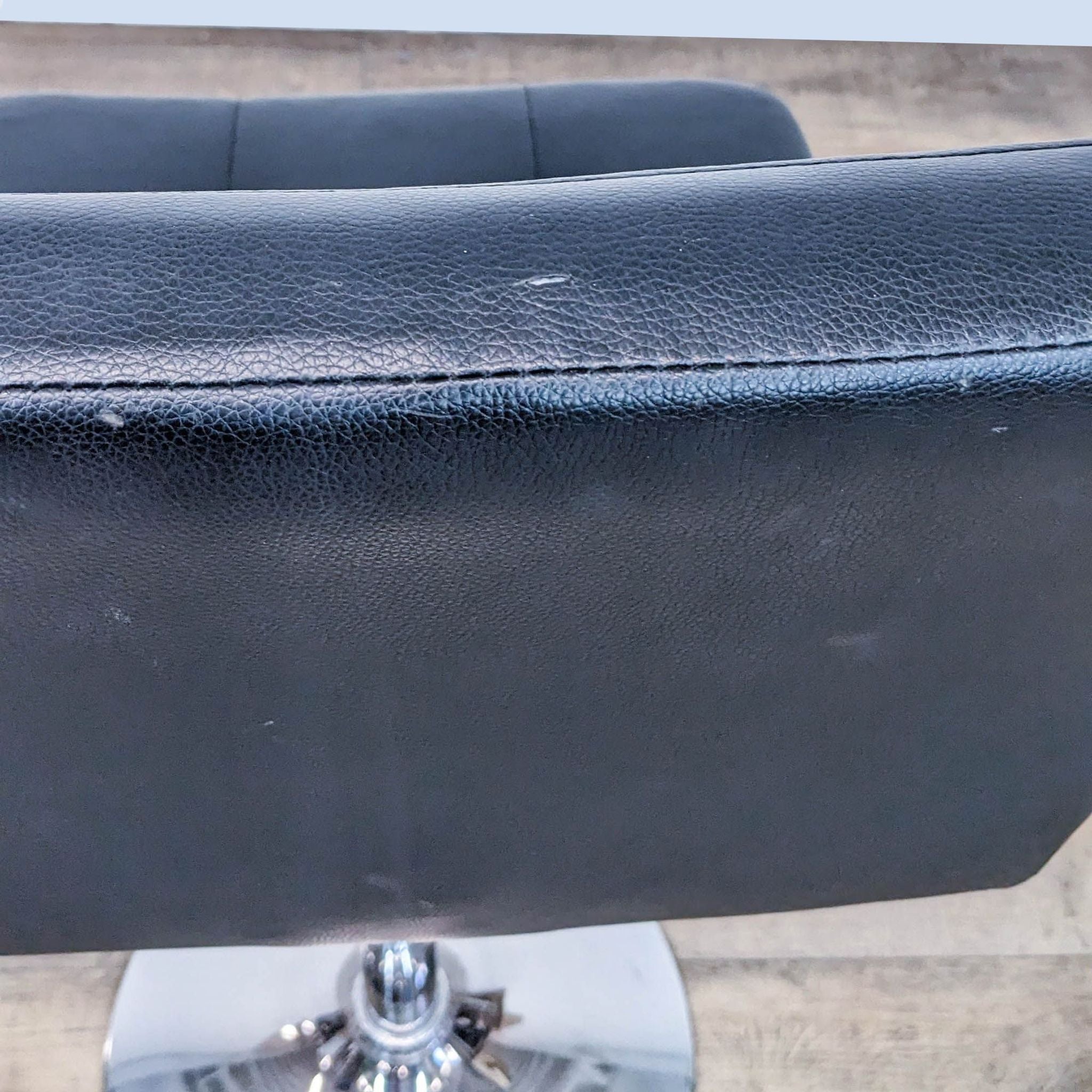 Close-up of a Reperch padded black leather look seat with signs of wear on a chrome gas lift frame.