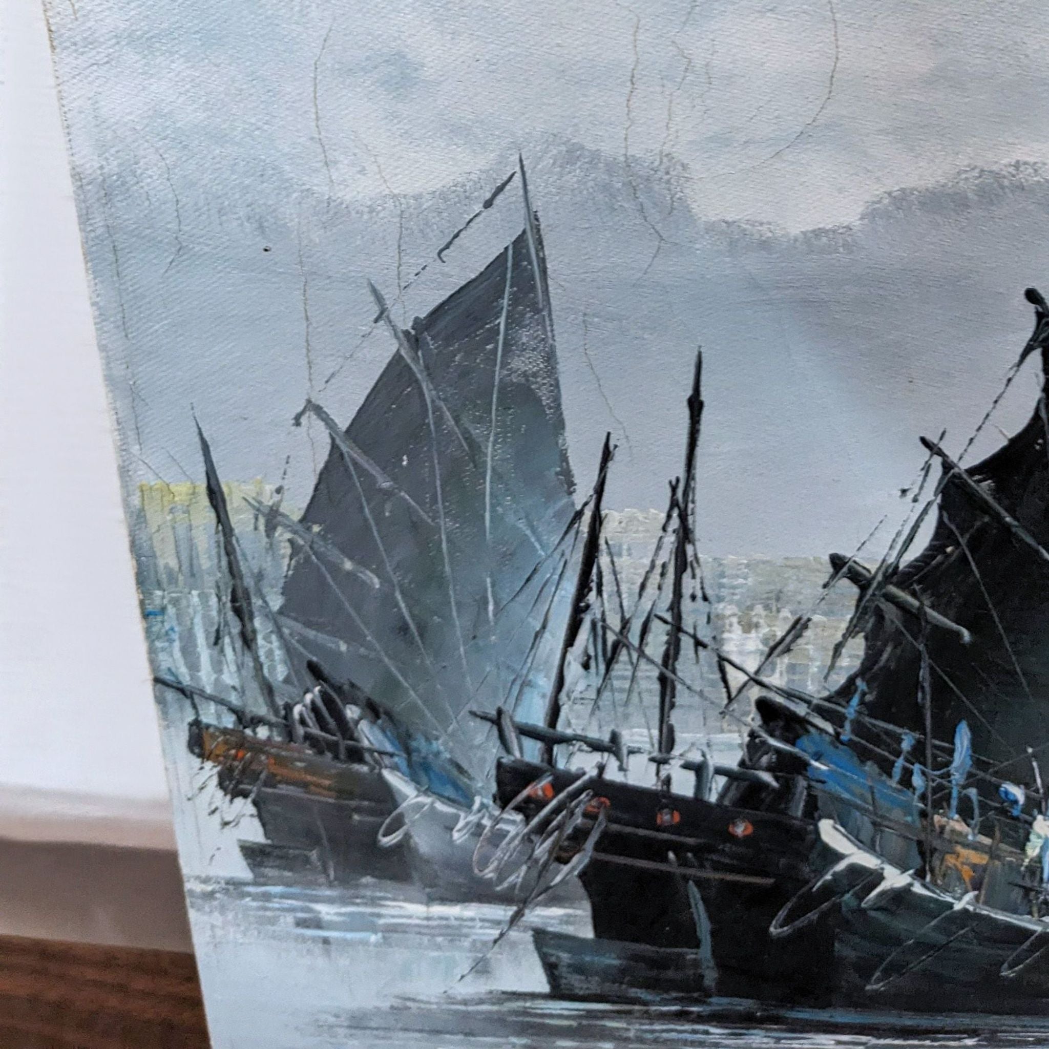 Close-up of sailboat painting showing detailed ships and signature of artist against a misty city backdrop.