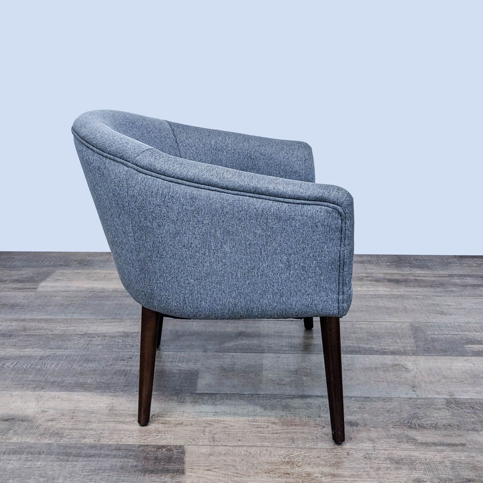 Reperch mid-century style dark gray upholstered armchair with a barrel back and tapered wood legs on a wooden floor.