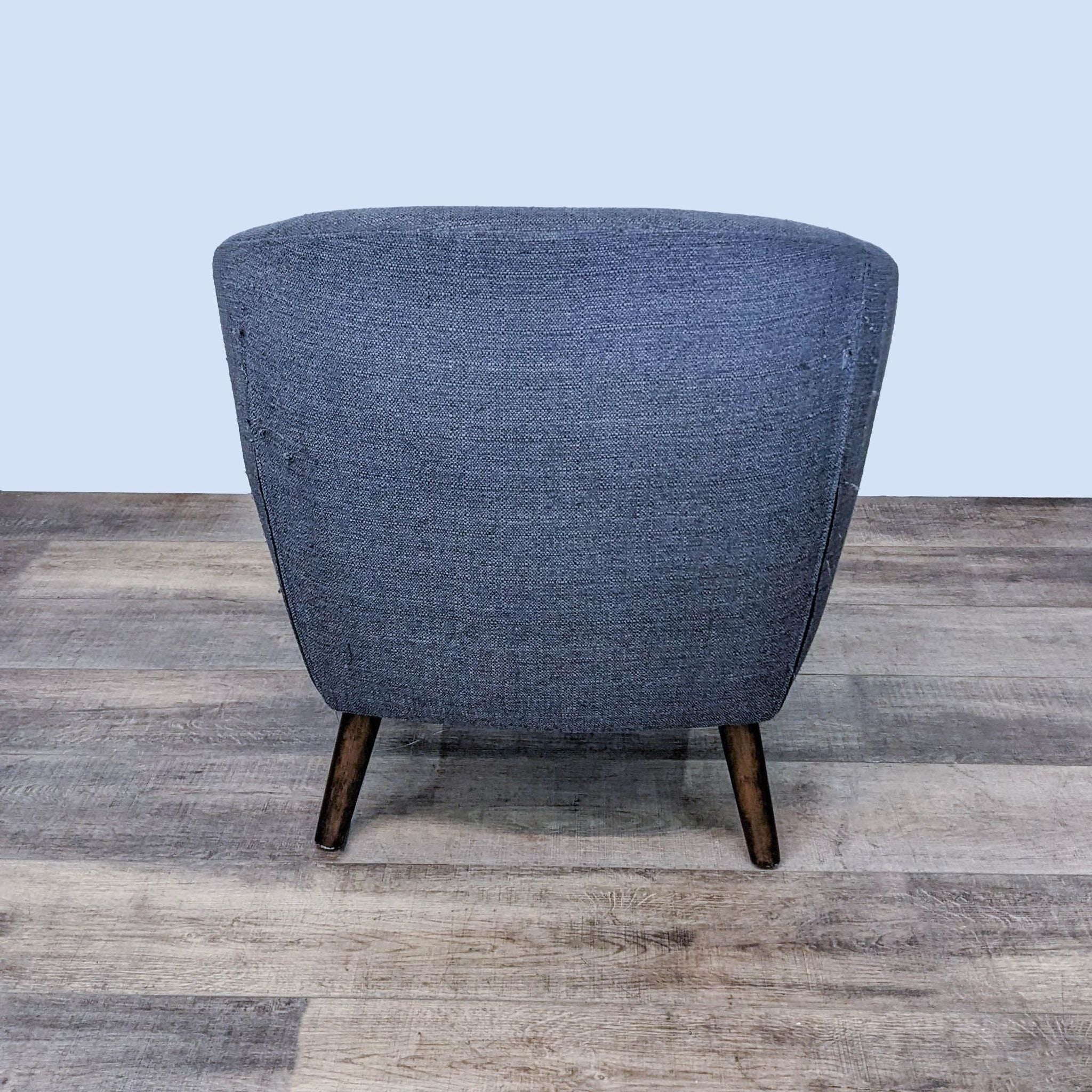 Rear view of a Reperch-brand mid-century style upholstered chair with tapered legs on a wood floor.