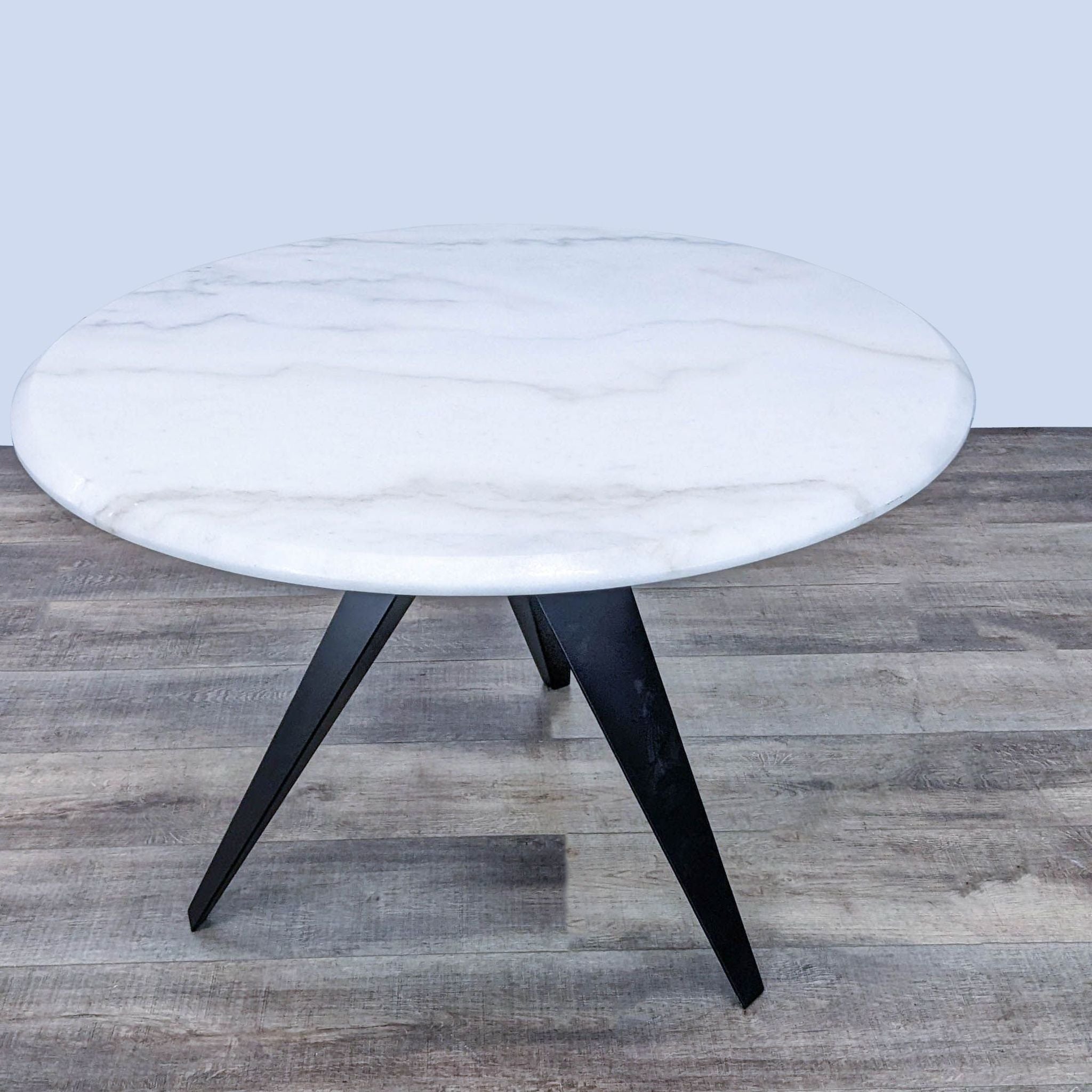 Minimalist Reperch dining table featuring a round marble surface with beveled edge and unique steel legs.