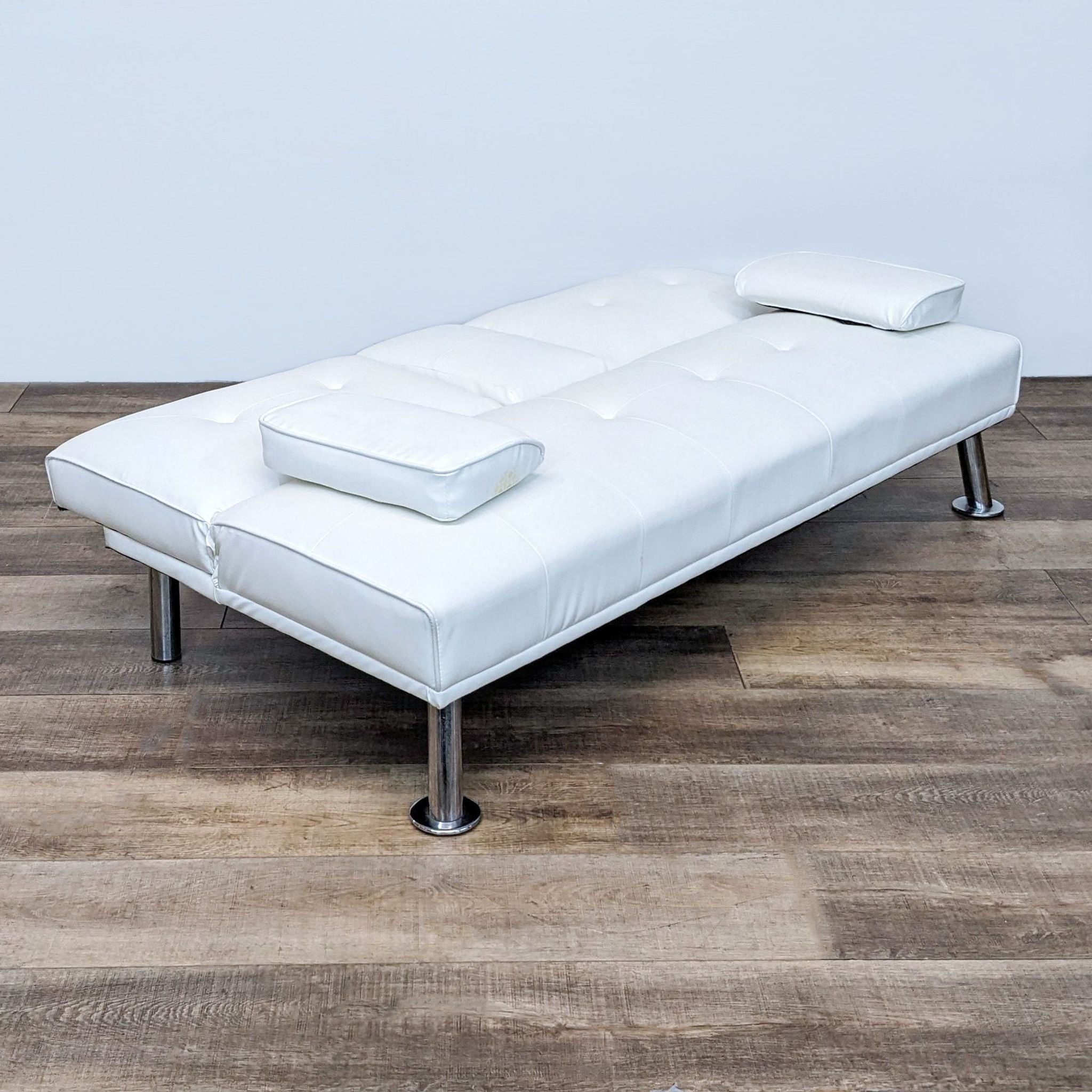 Alt text 2: White Reperch convertible sofa flattened into a bed with two cushions, on wooden flooring.