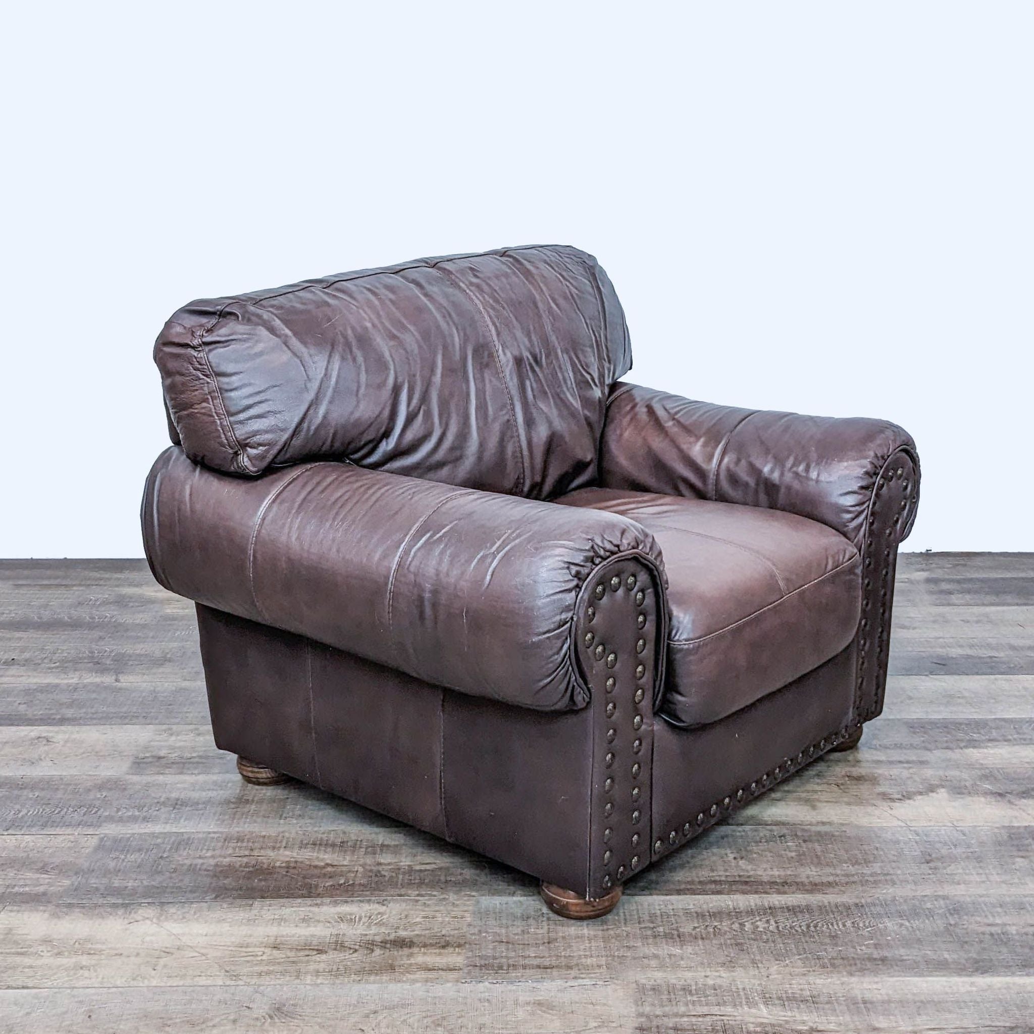 Reperch traditional leather lounge chair with rolled arms and nailhead trim on wood floor.
