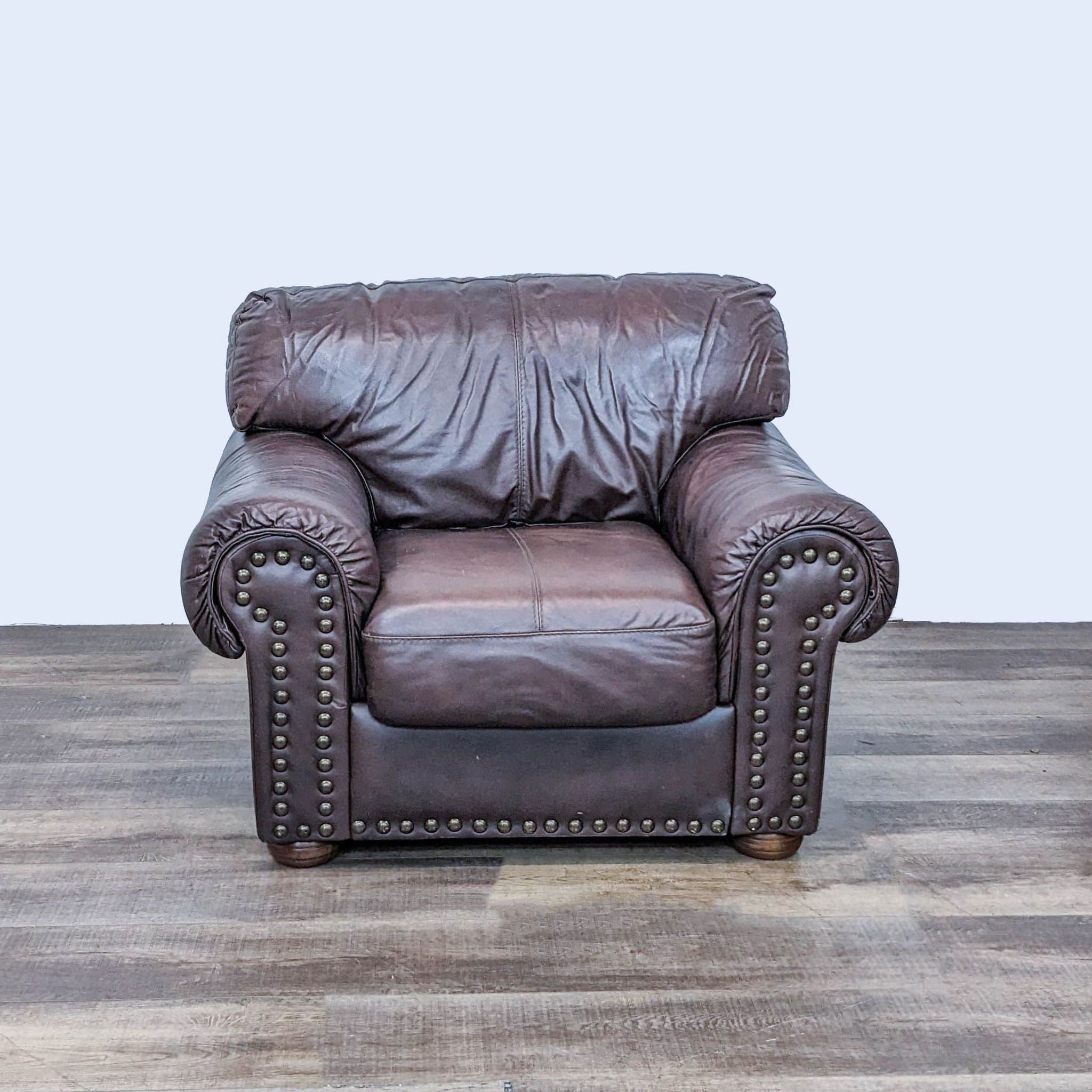 Brown leather Reperch lounge chair with matching footrest featuring nailhead accents and rolled arms against a neutral backdrop.