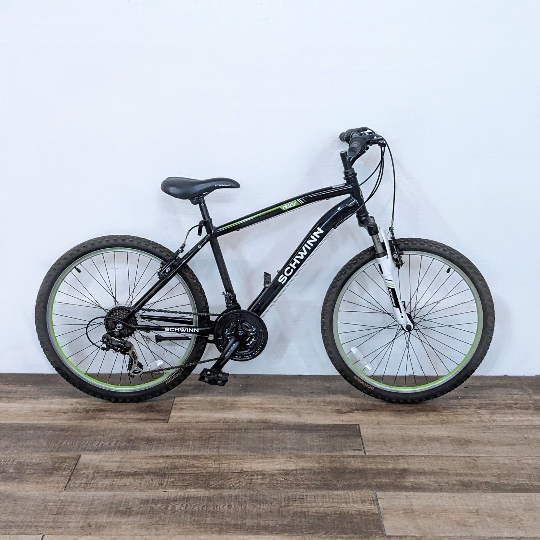 A durable Schwinn bicycle positioned against a white wall, showcasing its capability for rugged terrains with a sleek black and green design.