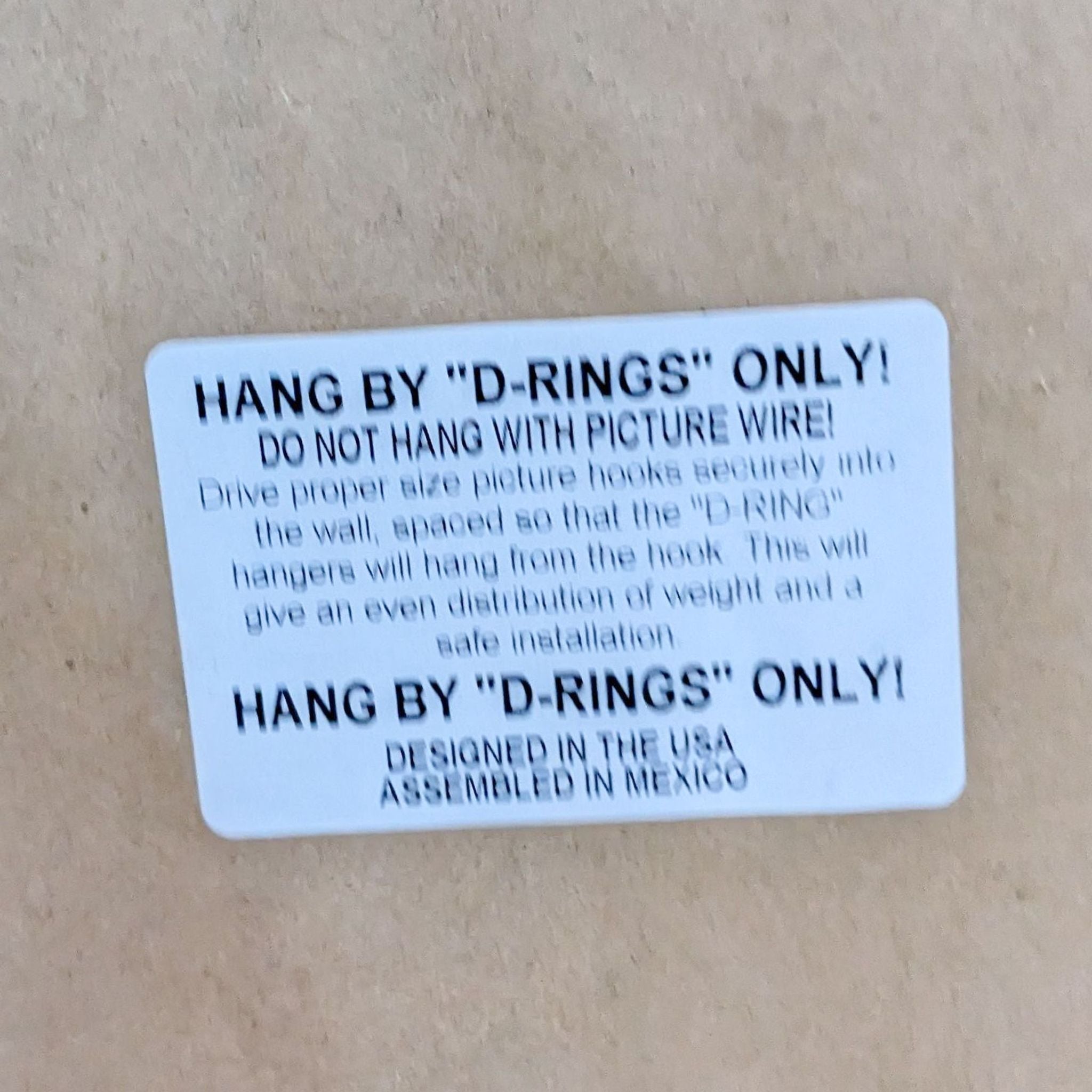 Close-up of a hanging instruction label on a Reperch rustic framed mirror, specifying to use "D-Rings" for mounting.