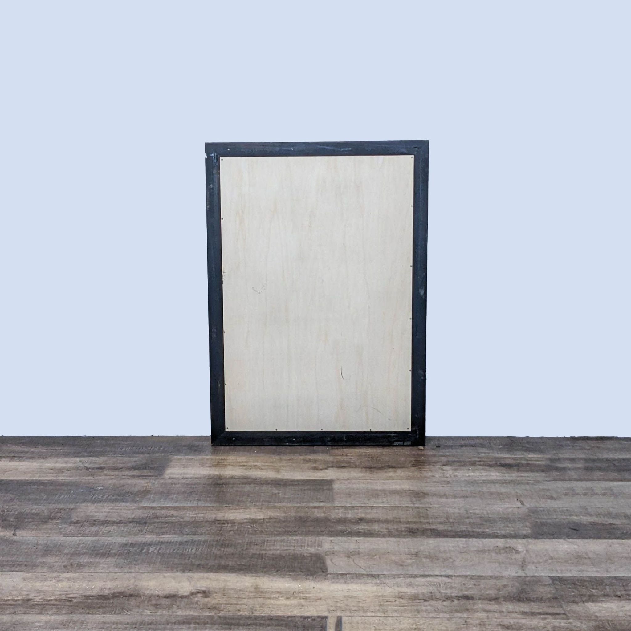 Rear view of Reperch wooden mirror, displaying sturdy back construction, against a grey wall on a wooden floor.