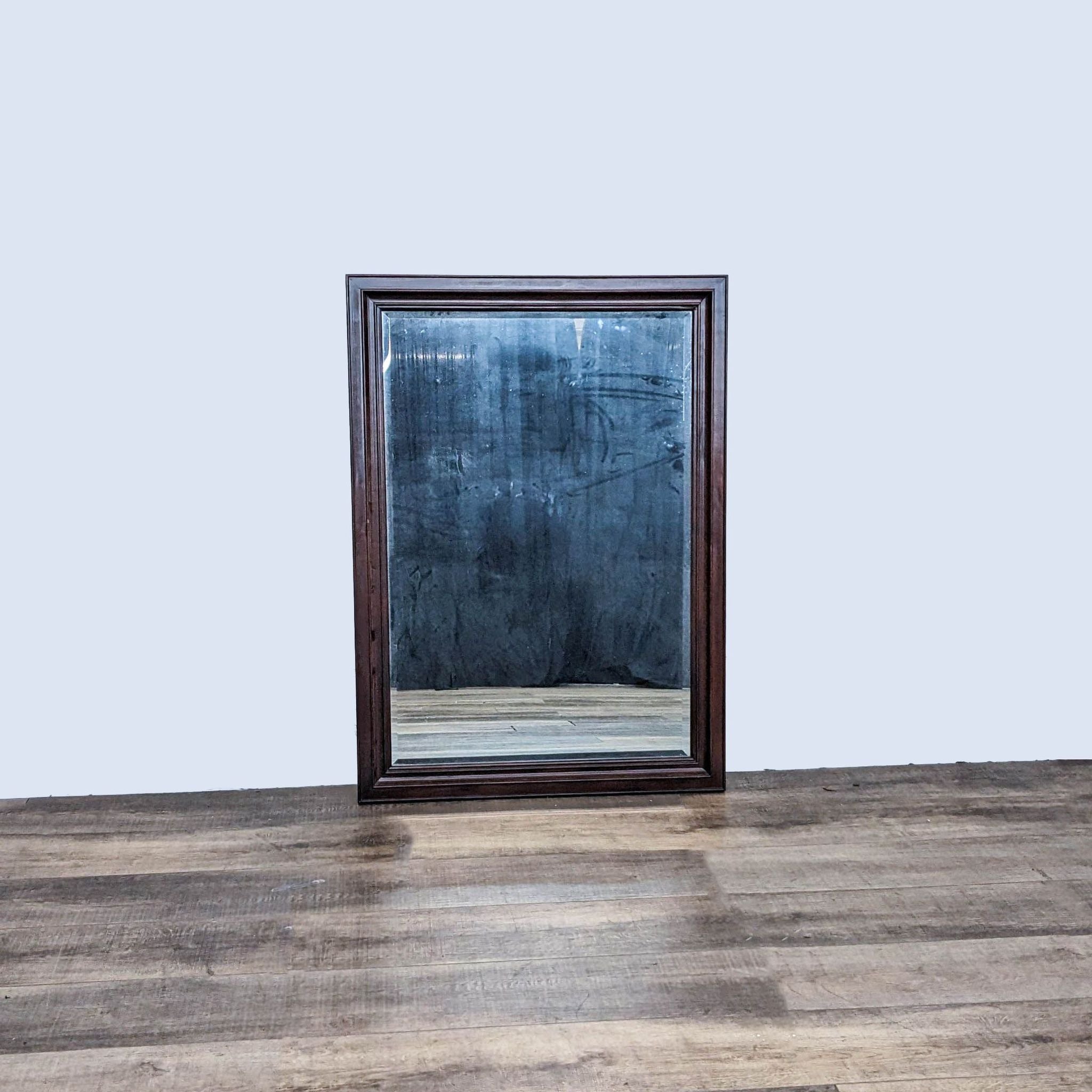Traditional Reperch wood-framed mirror with beveled edges, standing on a wooden floor against a grey wall.