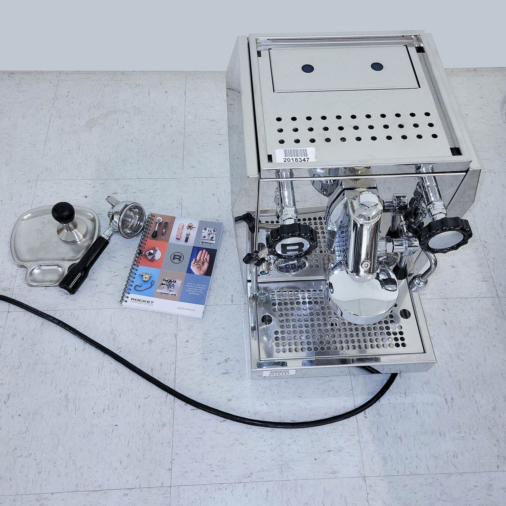Top view of a Rocket Espresso Machine alongside its accessories including a tamper, manual, and coffee filter on a white floor.