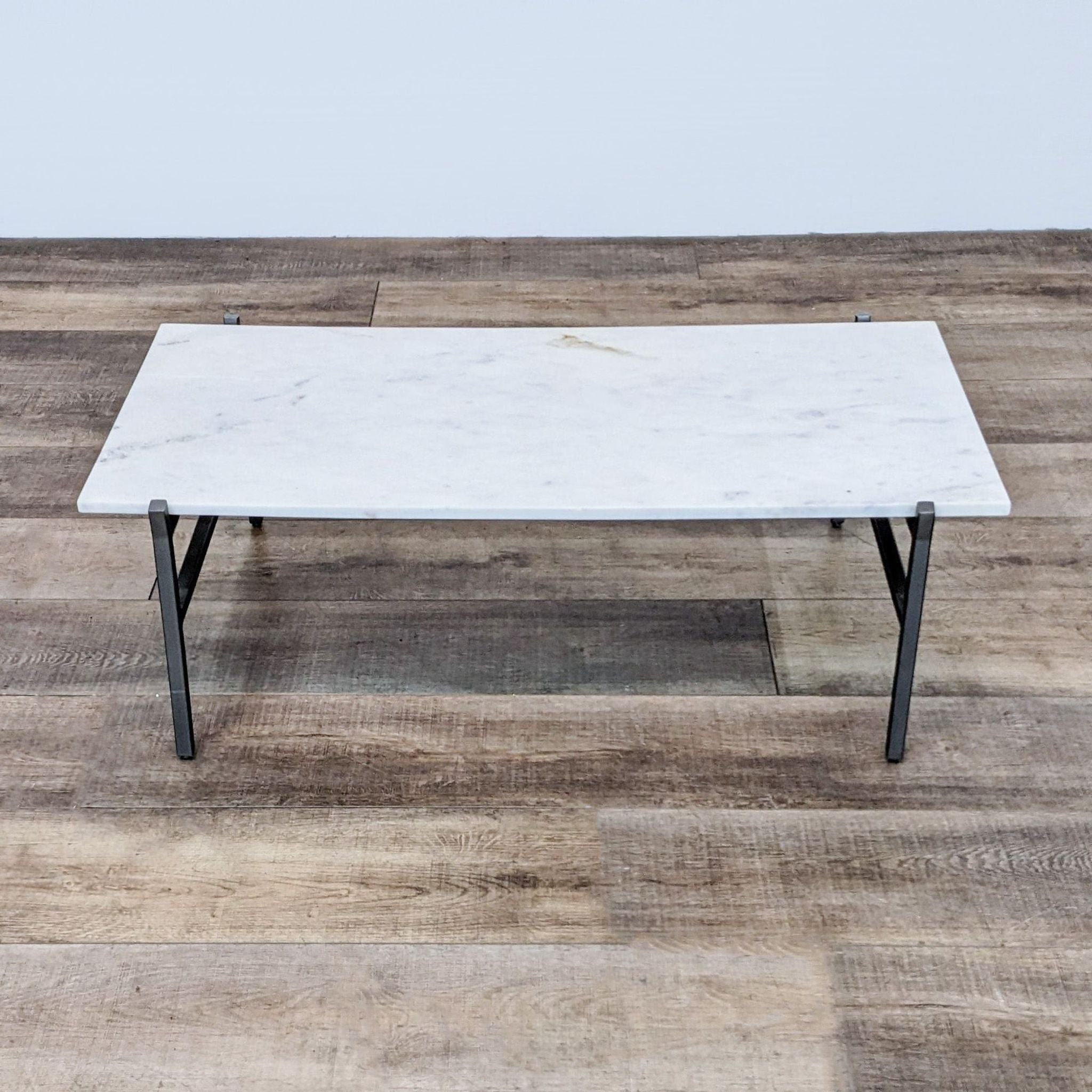 CB2 brand coffee table with a marble slab top and minimalist steel base on a wooden floor.