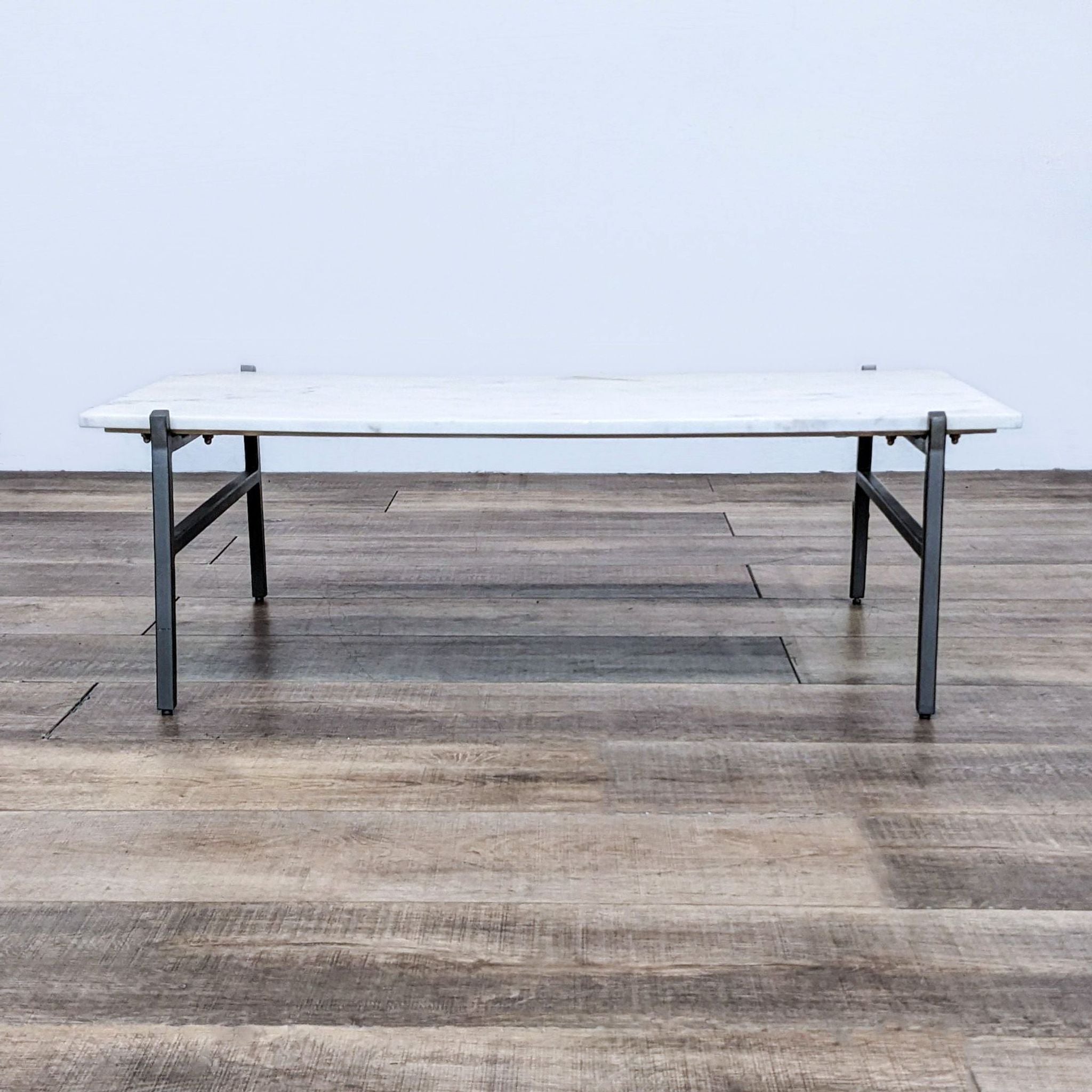 CB2 brand coffee table featuring a marble slab top on a steel base, shown against a wooden floor.
