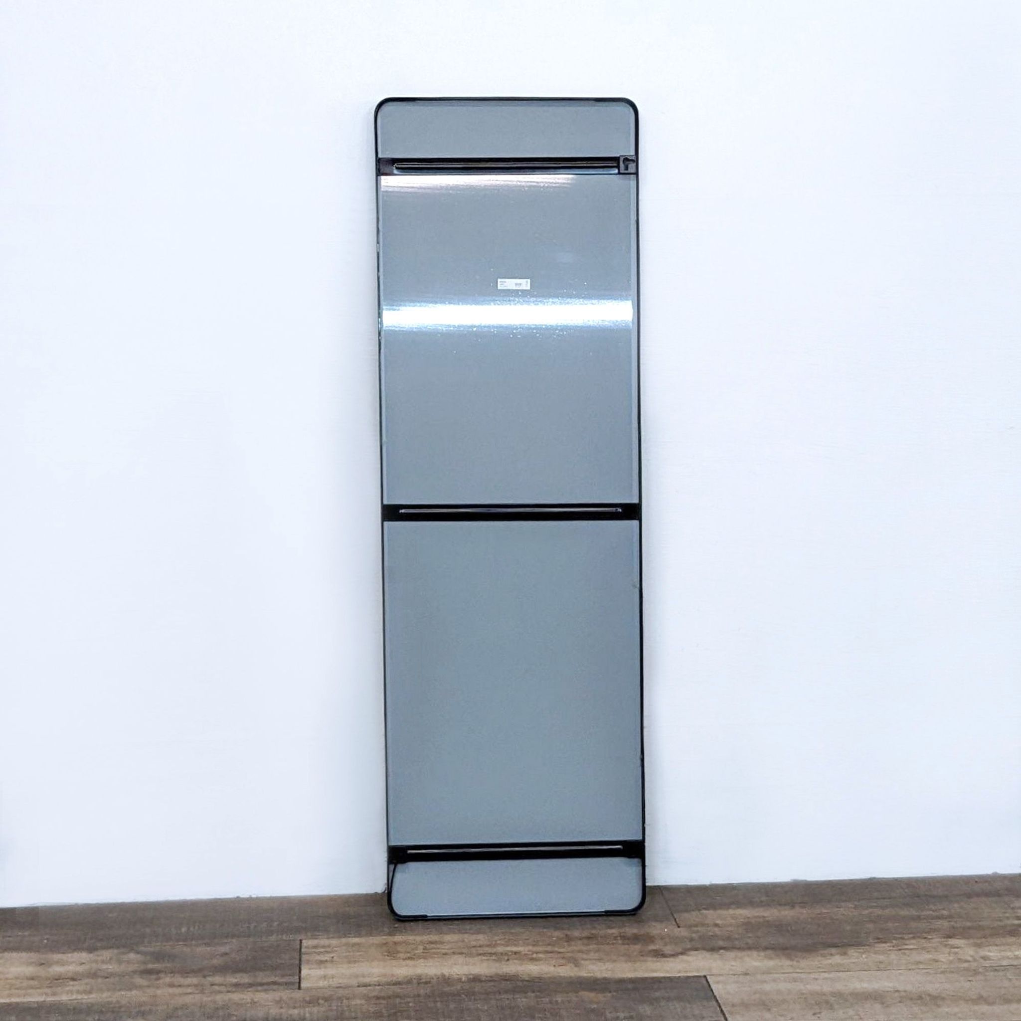 Image 3 alt: Rectangular full-length IKEA Grua mirror reflecting a white wall and a wooden floor, featuring a black frame with rounded corners.