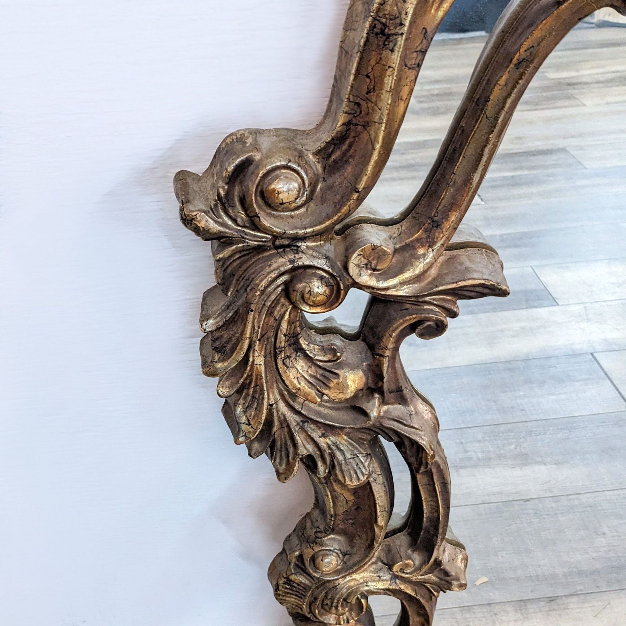 Close-up of a Reperch brand ornate mirror frame with gold accents and floral motifs.