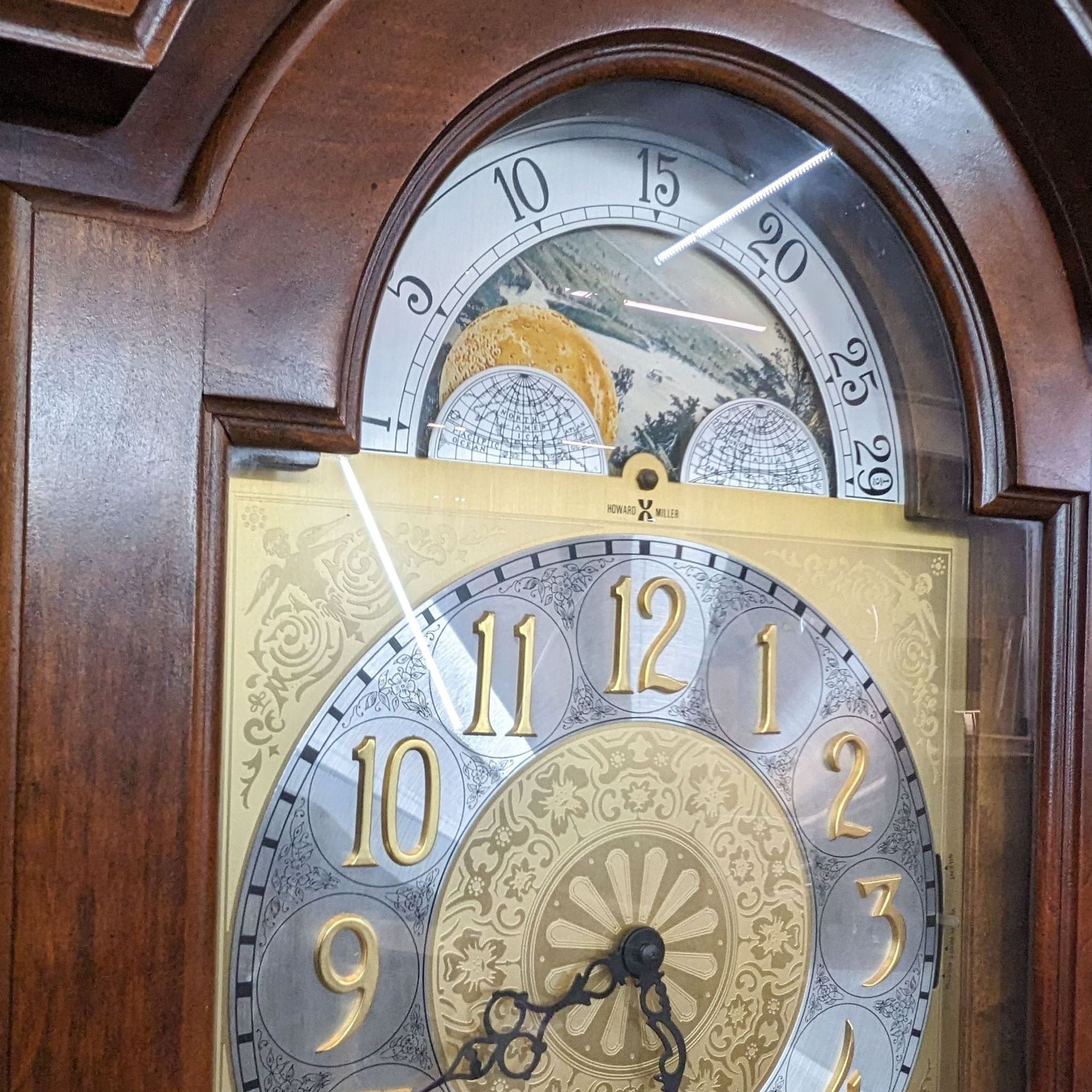 Close-up of Howard Miller Grandfather Clock showing detailed moon phase dial, decorative hands, and brass escutcheon on door.