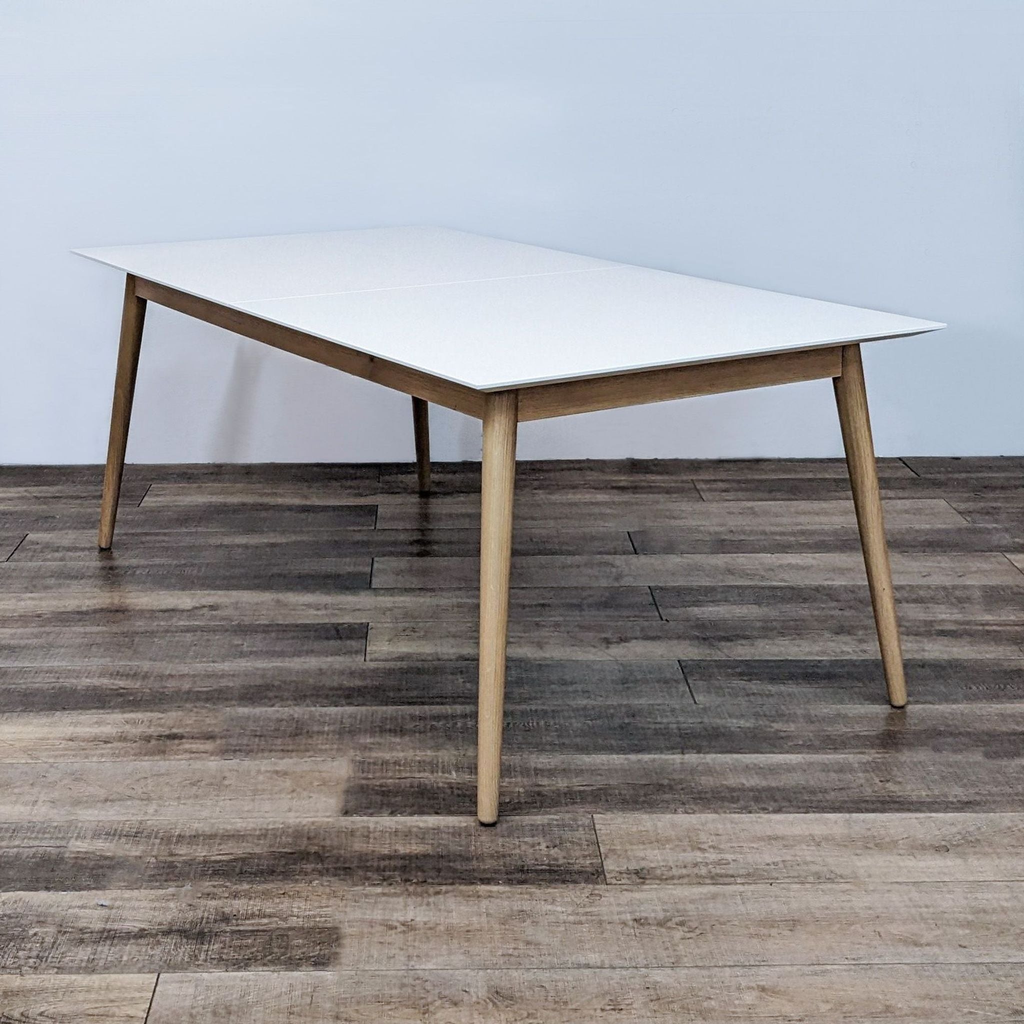 Modern BoConcept Milano extendable dining table with a white top and wooden legs on a wooden floor.