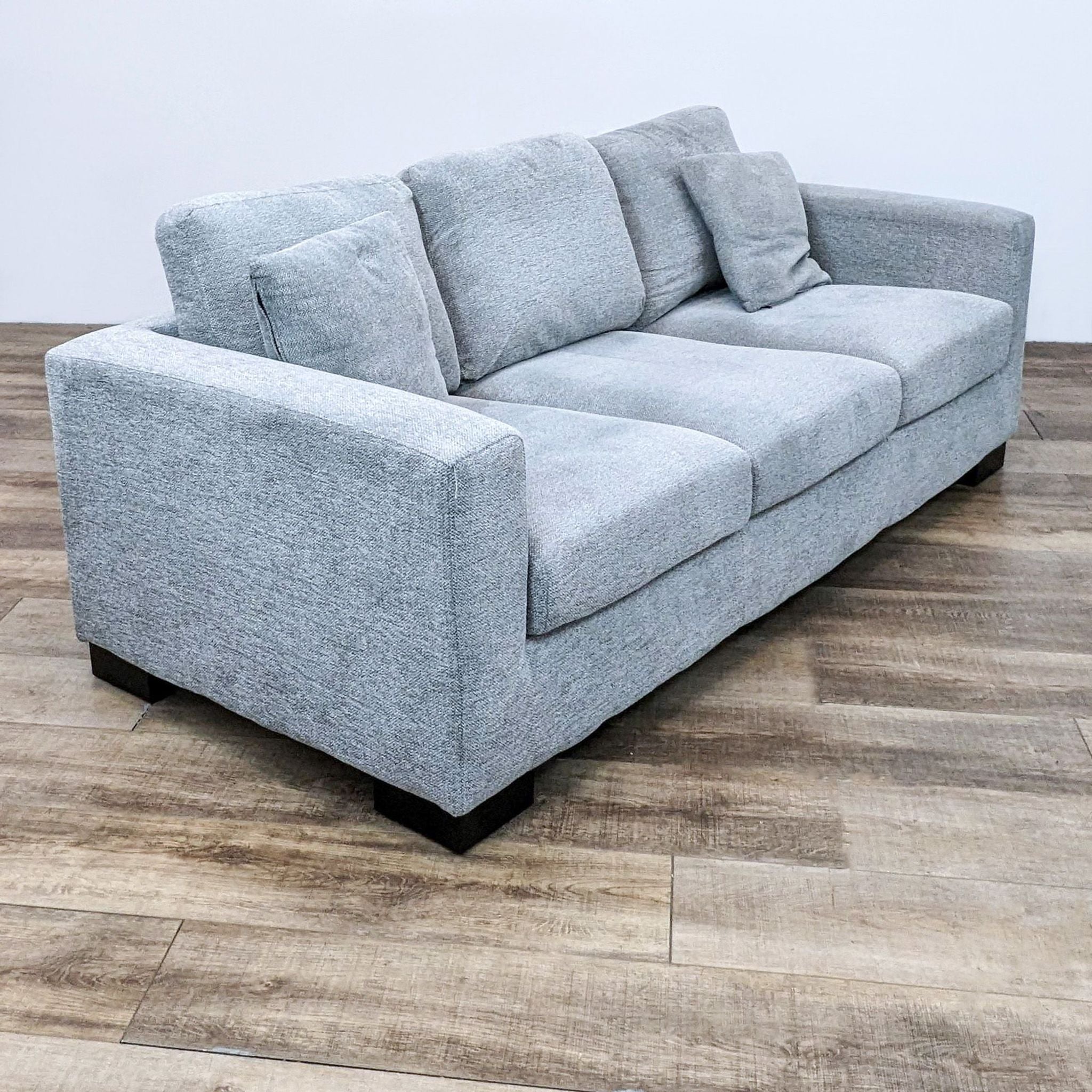 Three-seater Reperch sofa in gray with dark wood block feet and comfortable cushions, positioned on wooden flooring.