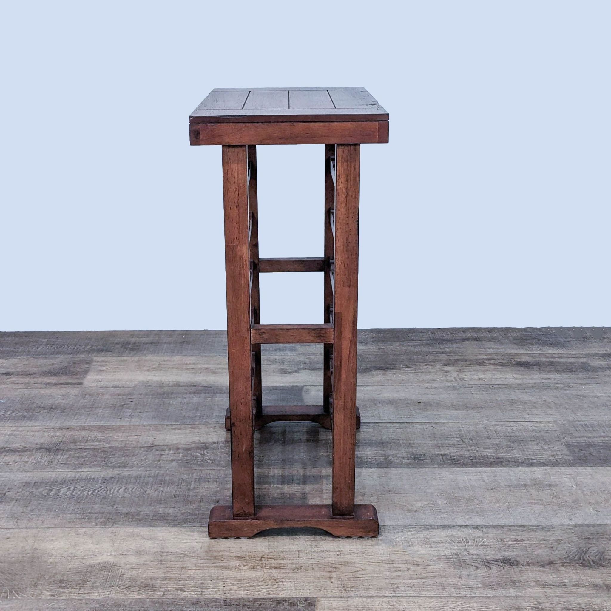Side view of Reperch wooden wine rack, sturdy frame with footrest, on gray floor.