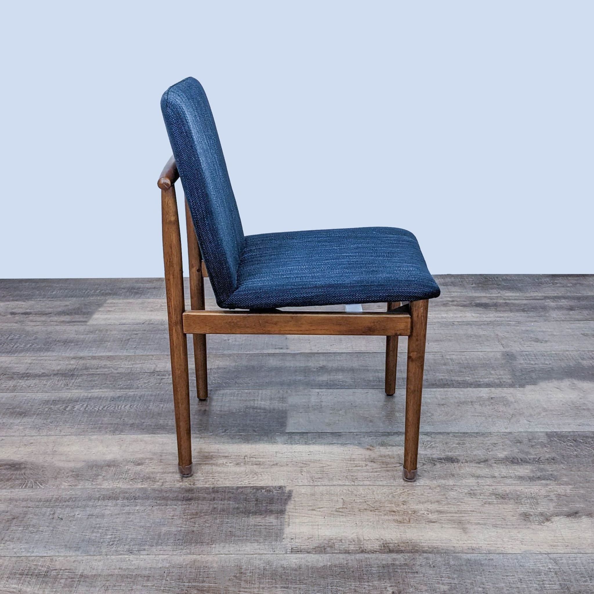Side view of a West Elm Modern Framework dining chair, showcasing the double T-back detail and blue upholstered seat against a wooden floor background.