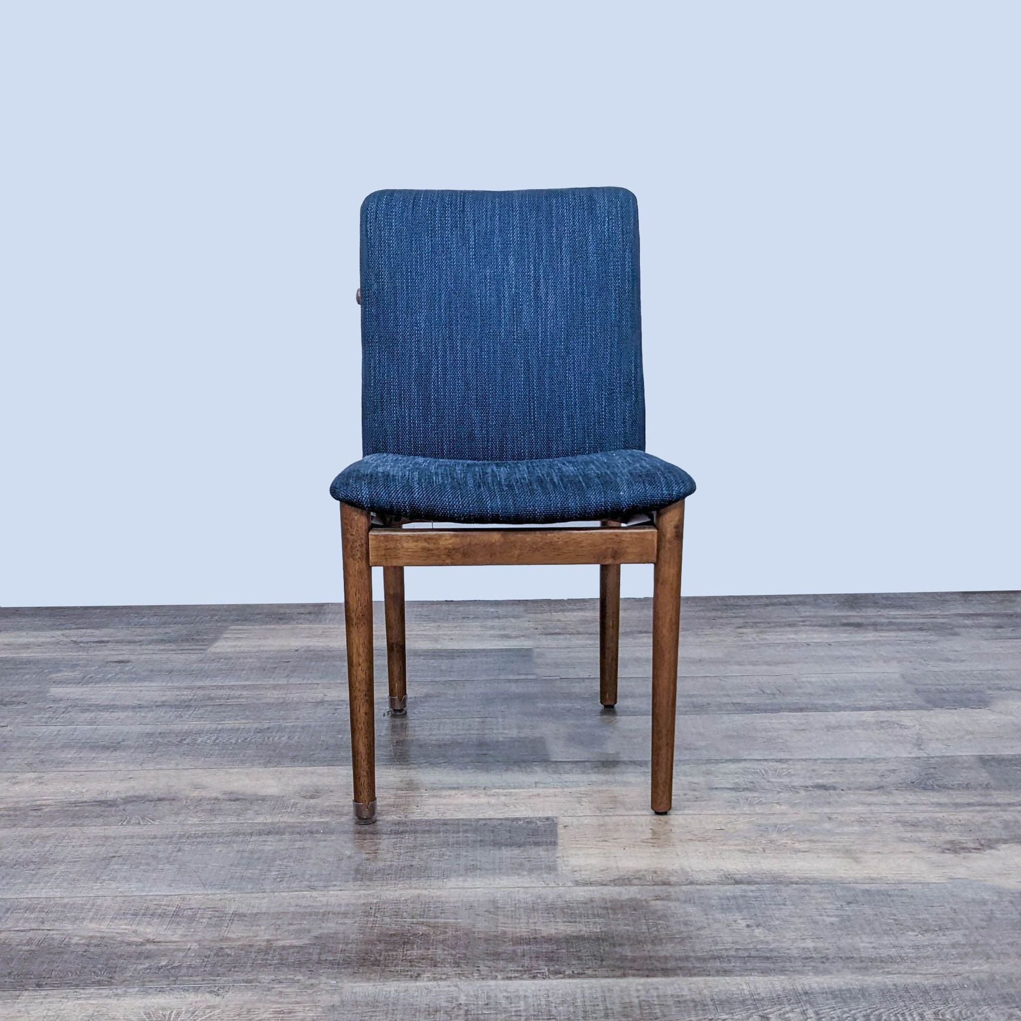 West Elm Modern Framework dining chair with denim-like blue fabric cushion and brown wooden frame, front view on a wooden floor.