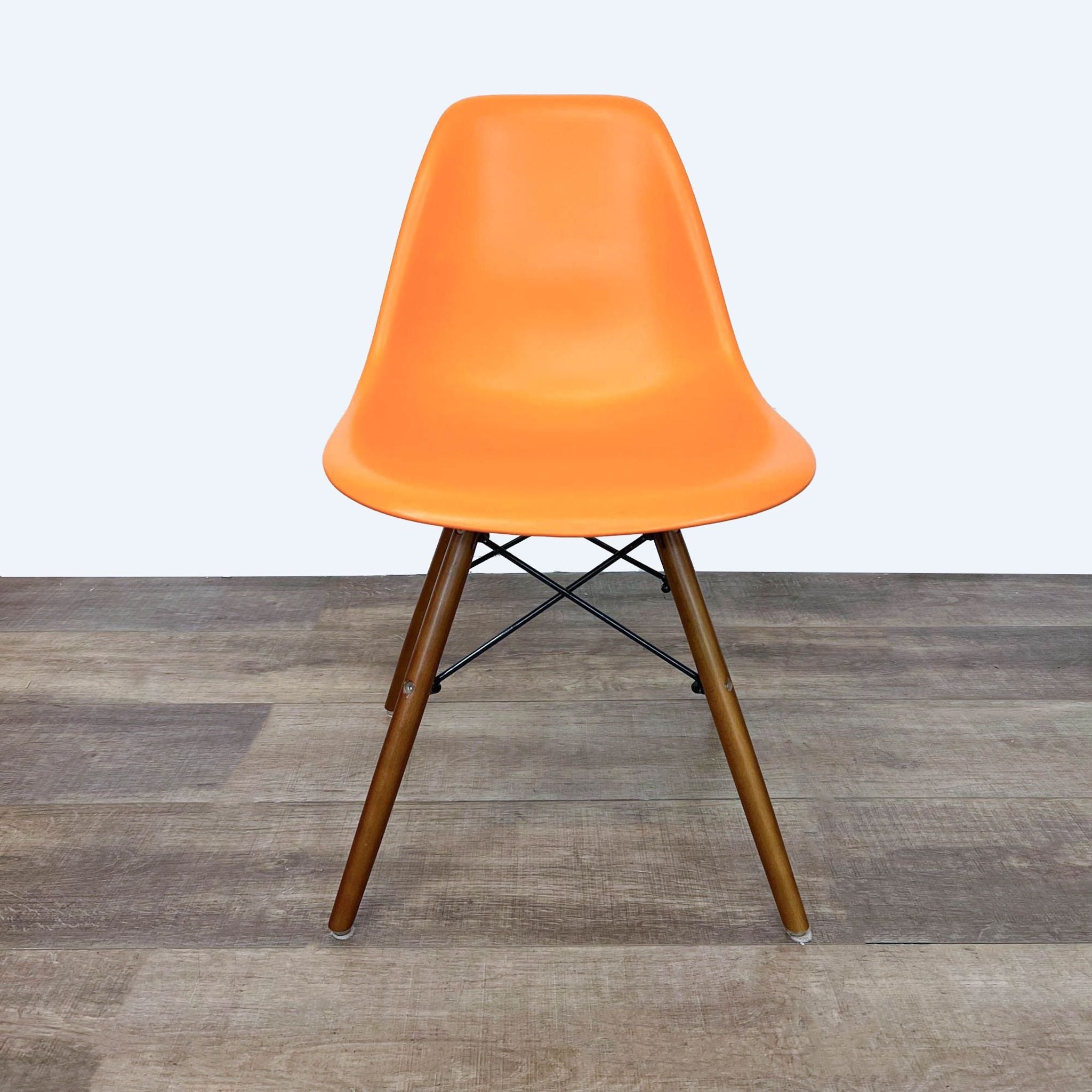 Reperch brand orange dining chair with ergonomic polypropylene seat and Eifel-style wooden legs on a hardwood floor.