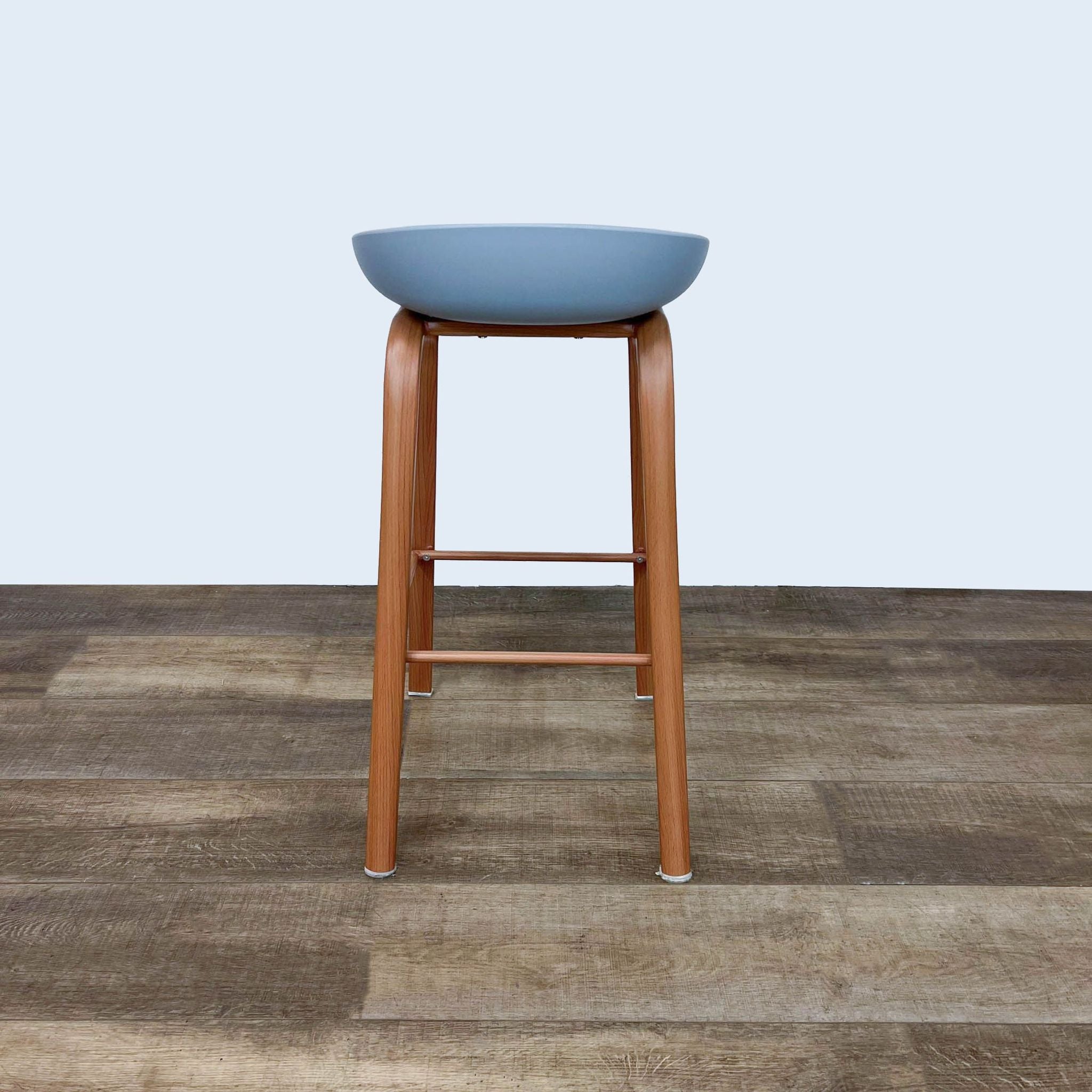 Gray Reperch barstool with plastic seat and wooden frame, on wooden floor.