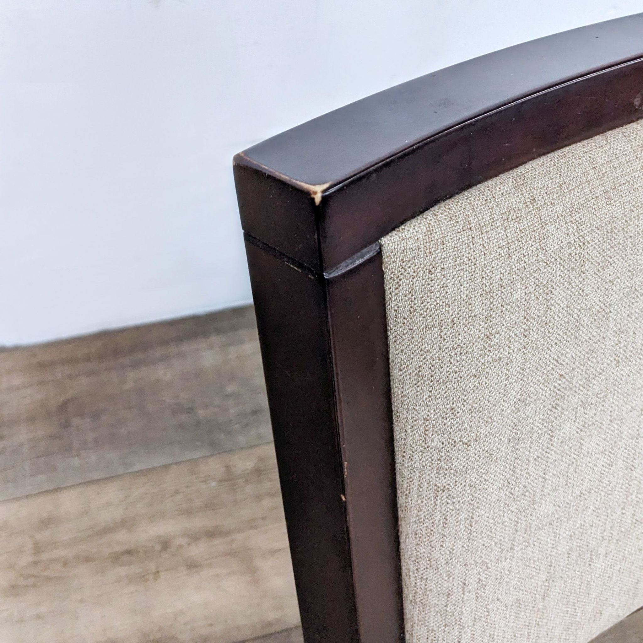 Close-up of a Sitcom dining chair corner with dark wood finish and neutral fabric upholstery.