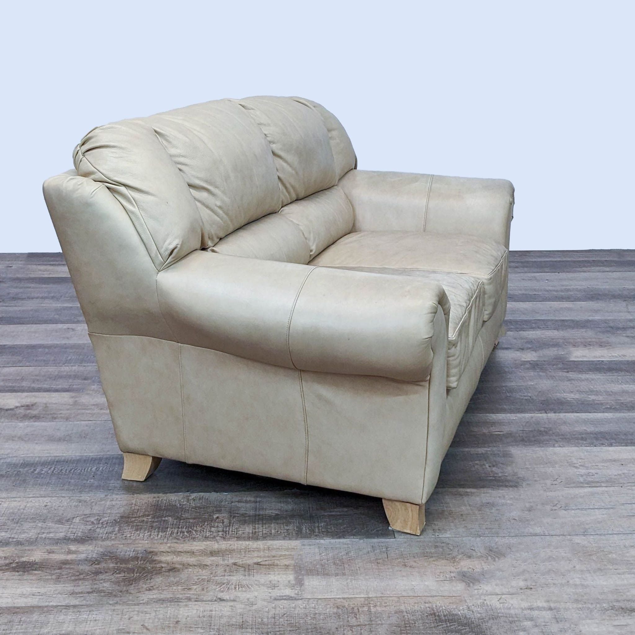 Reperch tan leather loveseat showcasing high back and side, featuring lumbar support and light finish wooden feet, angled view.