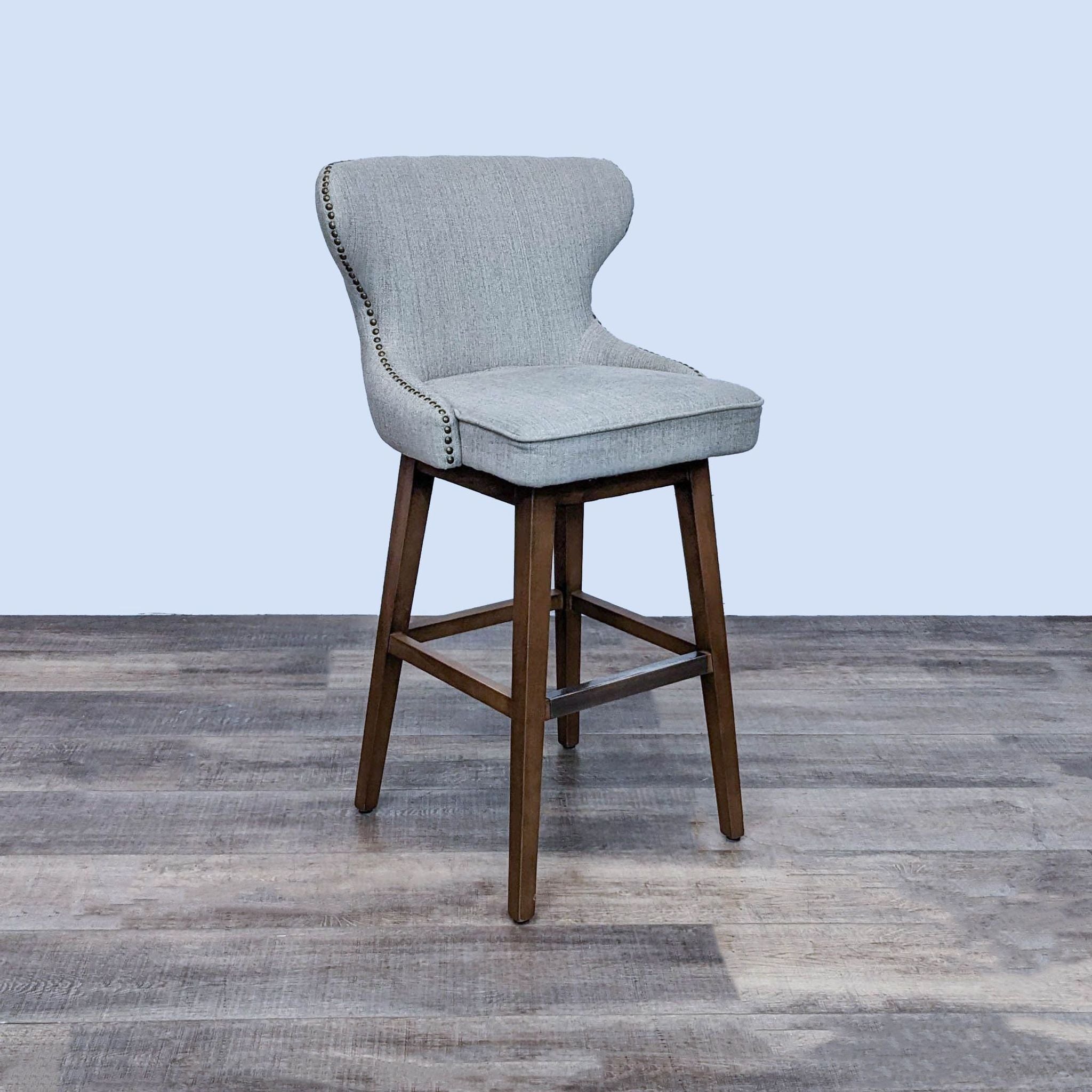 Neutral-colored fabric bar stool with tufted back and nailhead details on a solid wood frame, by Reperch, rear view.