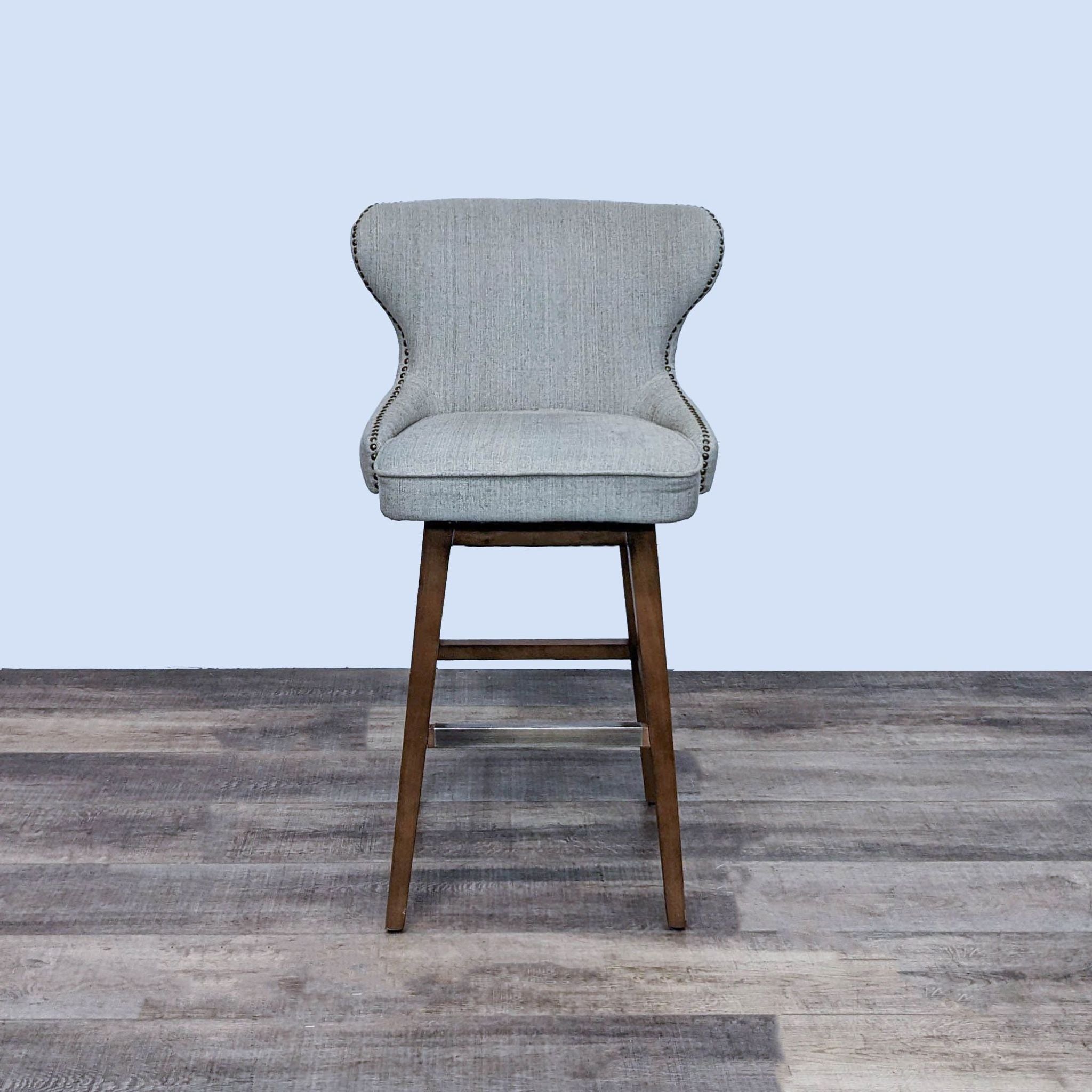 Neutral-colored tufted fabric bar stool with nailhead trim and wooden legs by Reperch, front view.