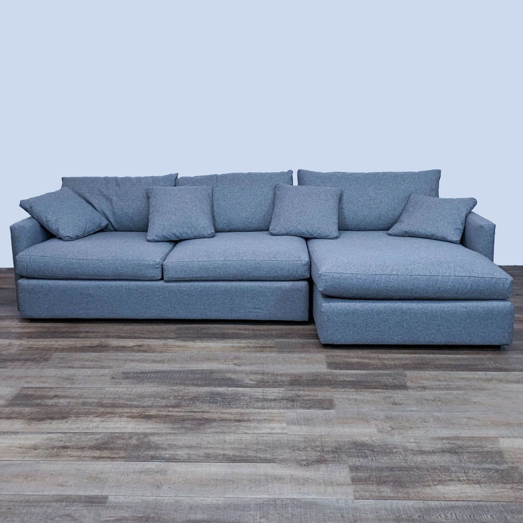 Crate & Barrel sectional sofa in a blue fabric with plush cushions and a chaise lounge, on a wooden floor.