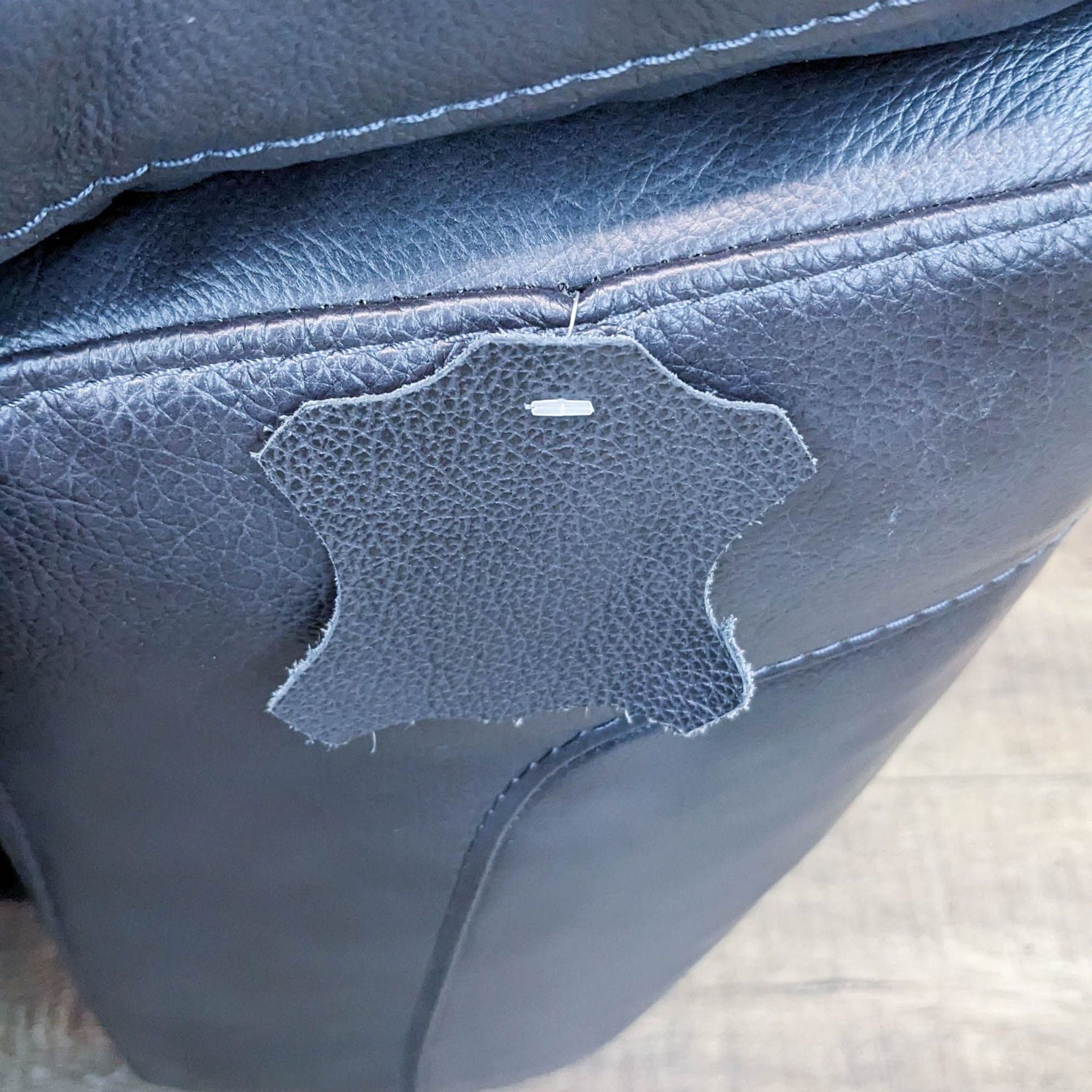Alt text: Close-up of a damaged area on a Reperch brand leather sofa showing torn upholstery with quilted side stitching detail.