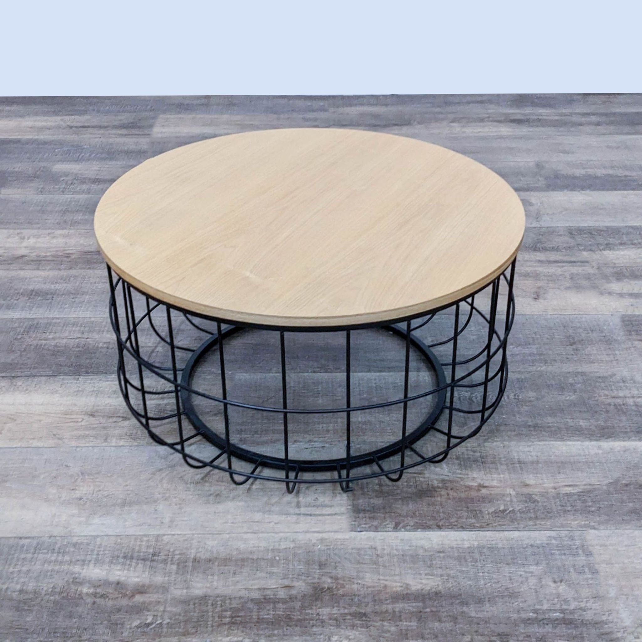 Wooden circular coffee table with a metal grid base by Oliver Space, showcased on a gray floor.