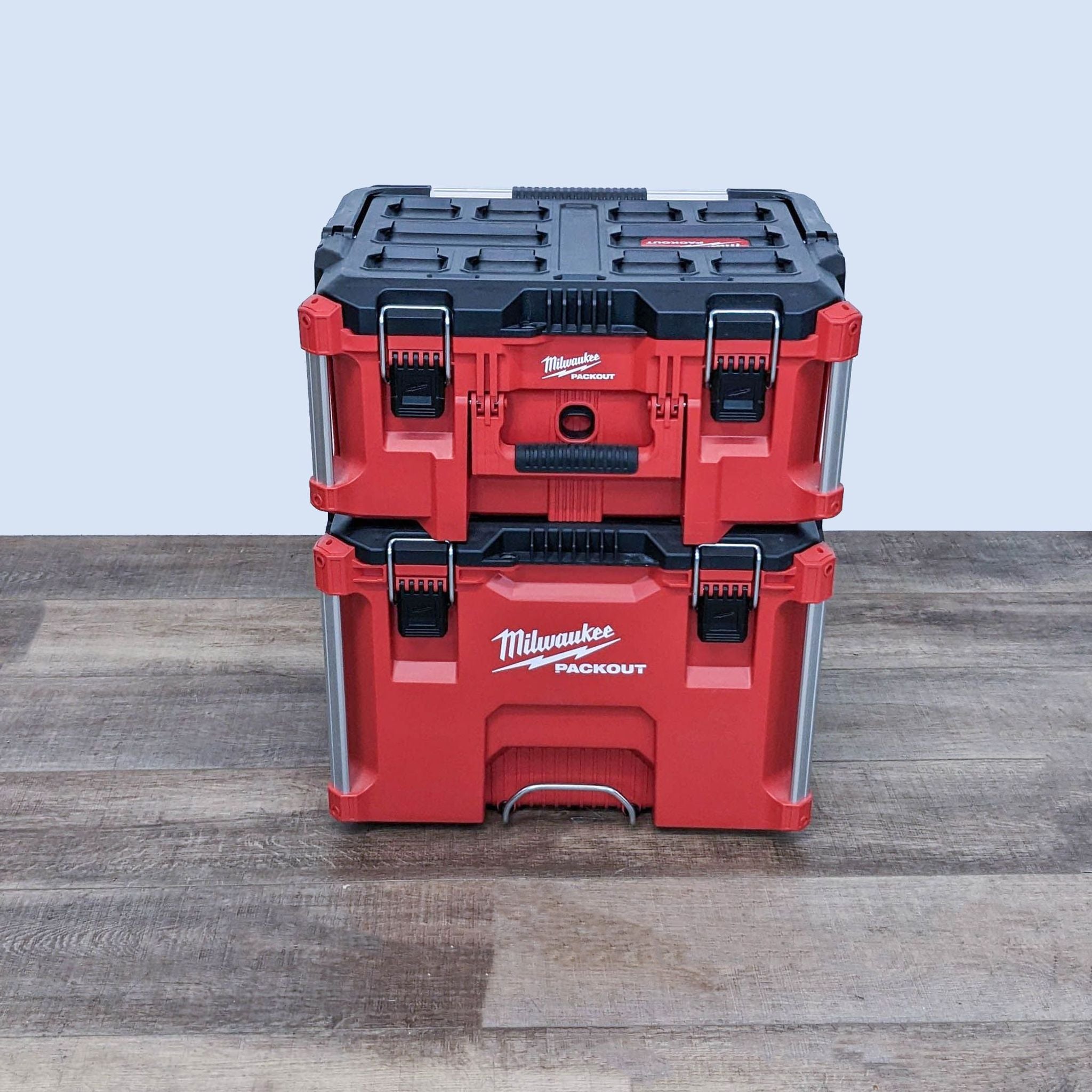 Stacked Milwaukee PACKOUT tool storage system with telescoping handle and durable latches on a wooden floor.