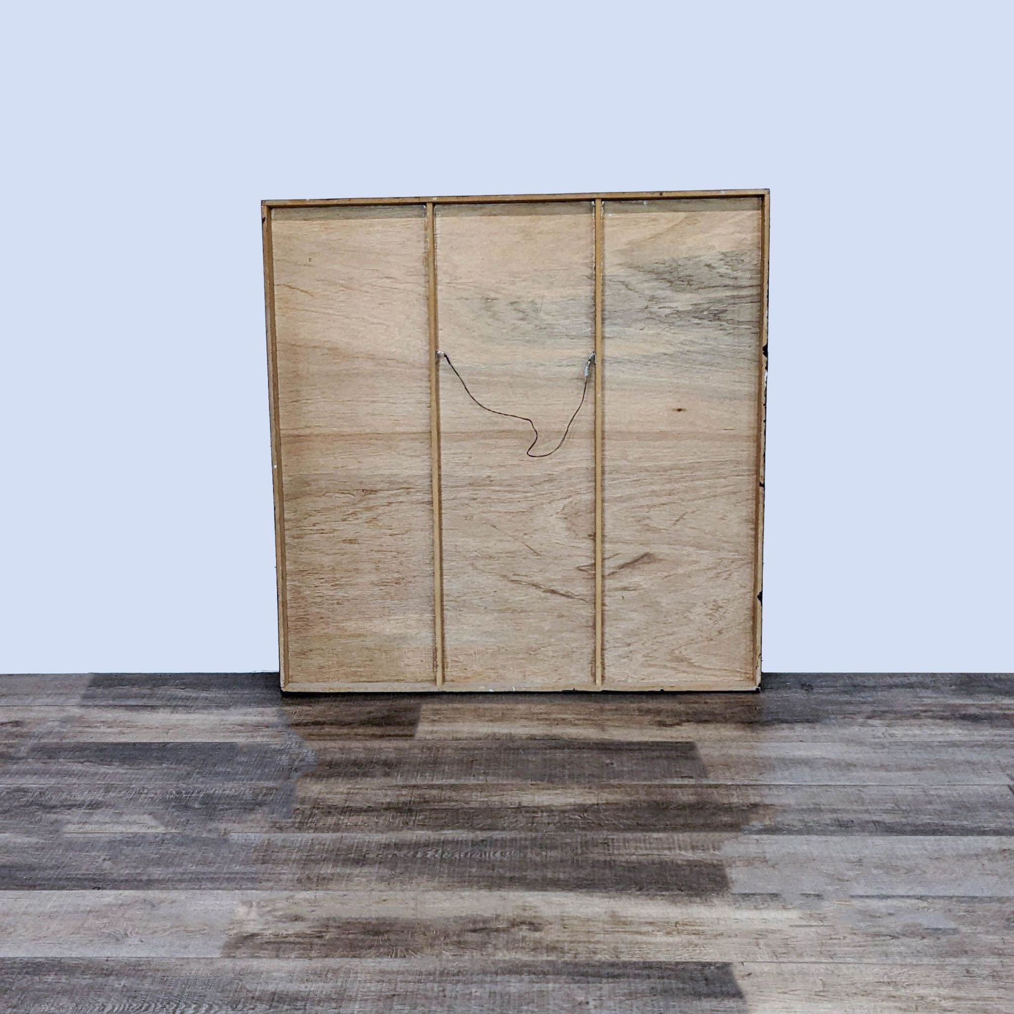 Reperch artwork's rear view, showing plain wood canvas stretcher with wire, standing on a wooden floor against a grey wall.