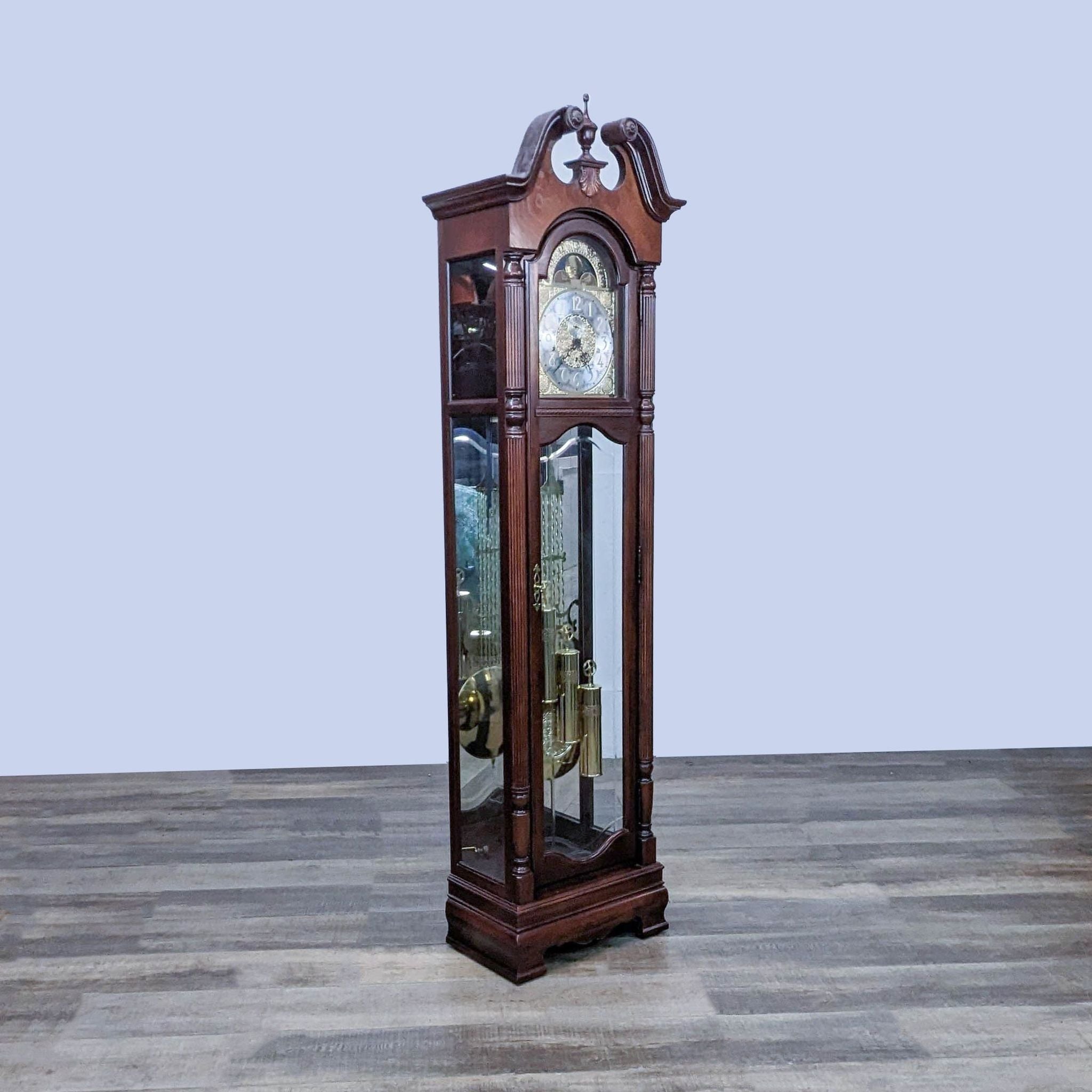 Side view of a Howard Miller wooden grandfather clock showcasing its pendulum and weights, on a wooden floor.