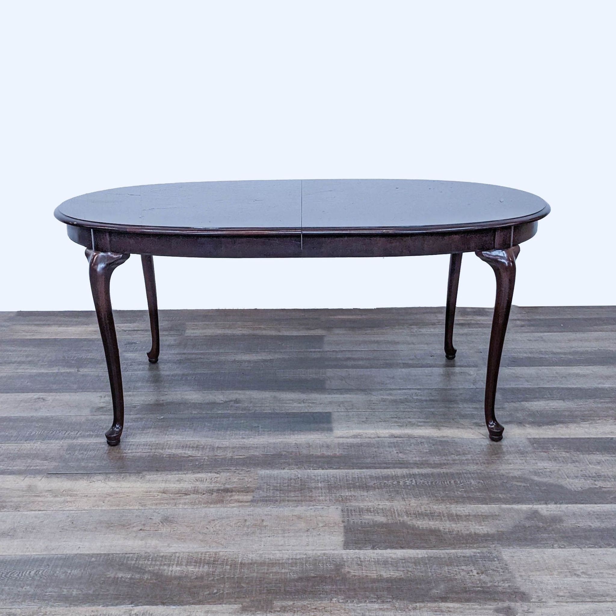 Elegant dark wood Ethan Allen extendable dining table from a 7-piece set, without chairs, on a hardwood floor.