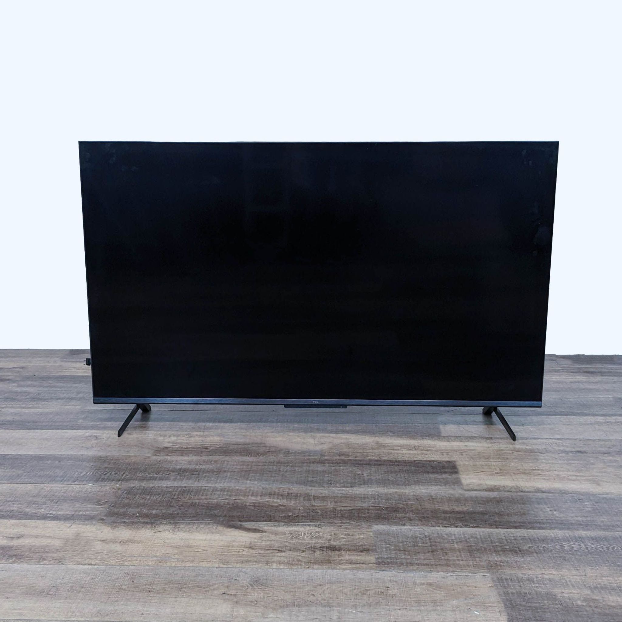 TCL Full HD Smart TV turned off, showcasing a sleek design and simple stands on a wooden floor.