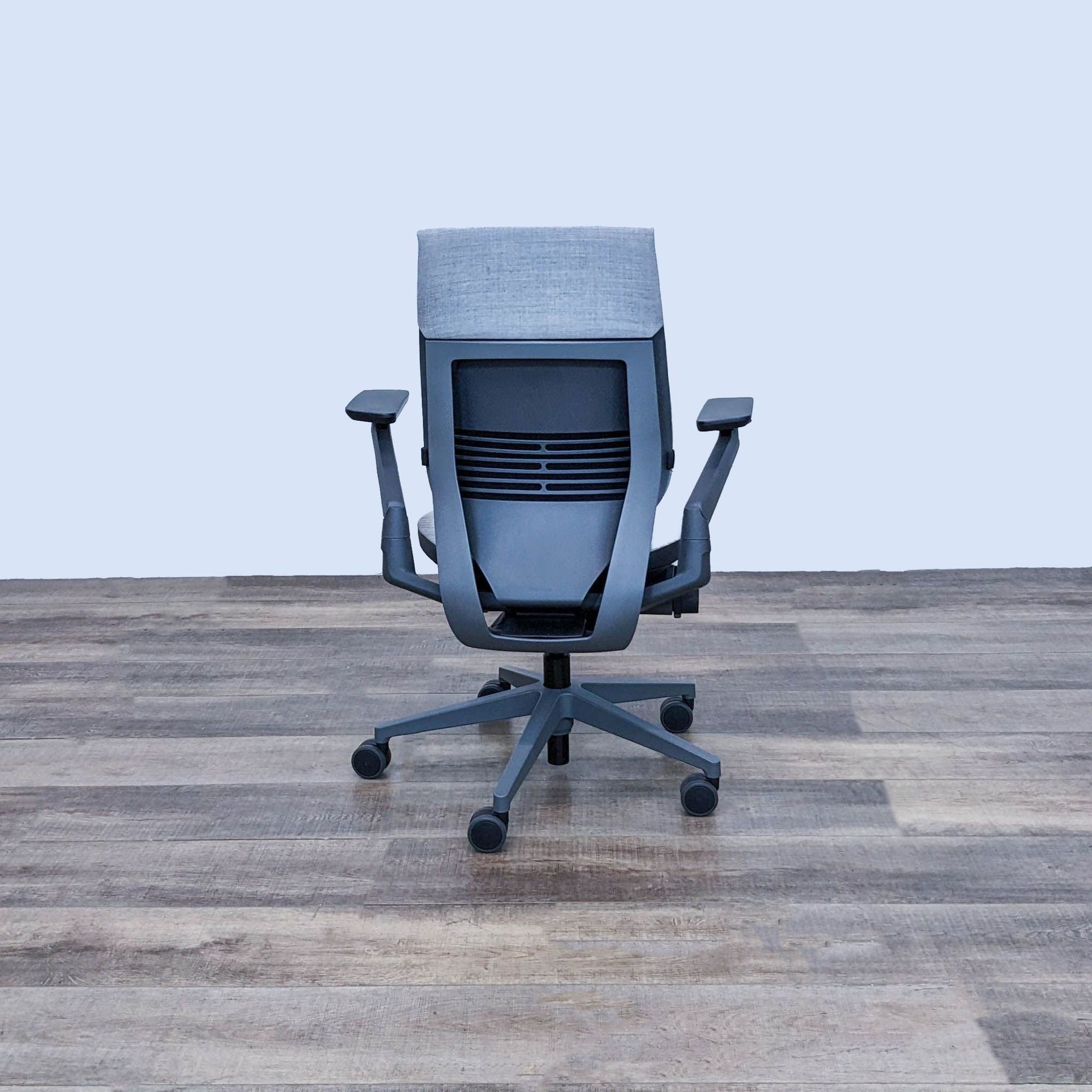 A rear view of a Steelcase Gesture chair showcasing the shell back, 4-position recline lock, and wheels suitable for hard flooring.