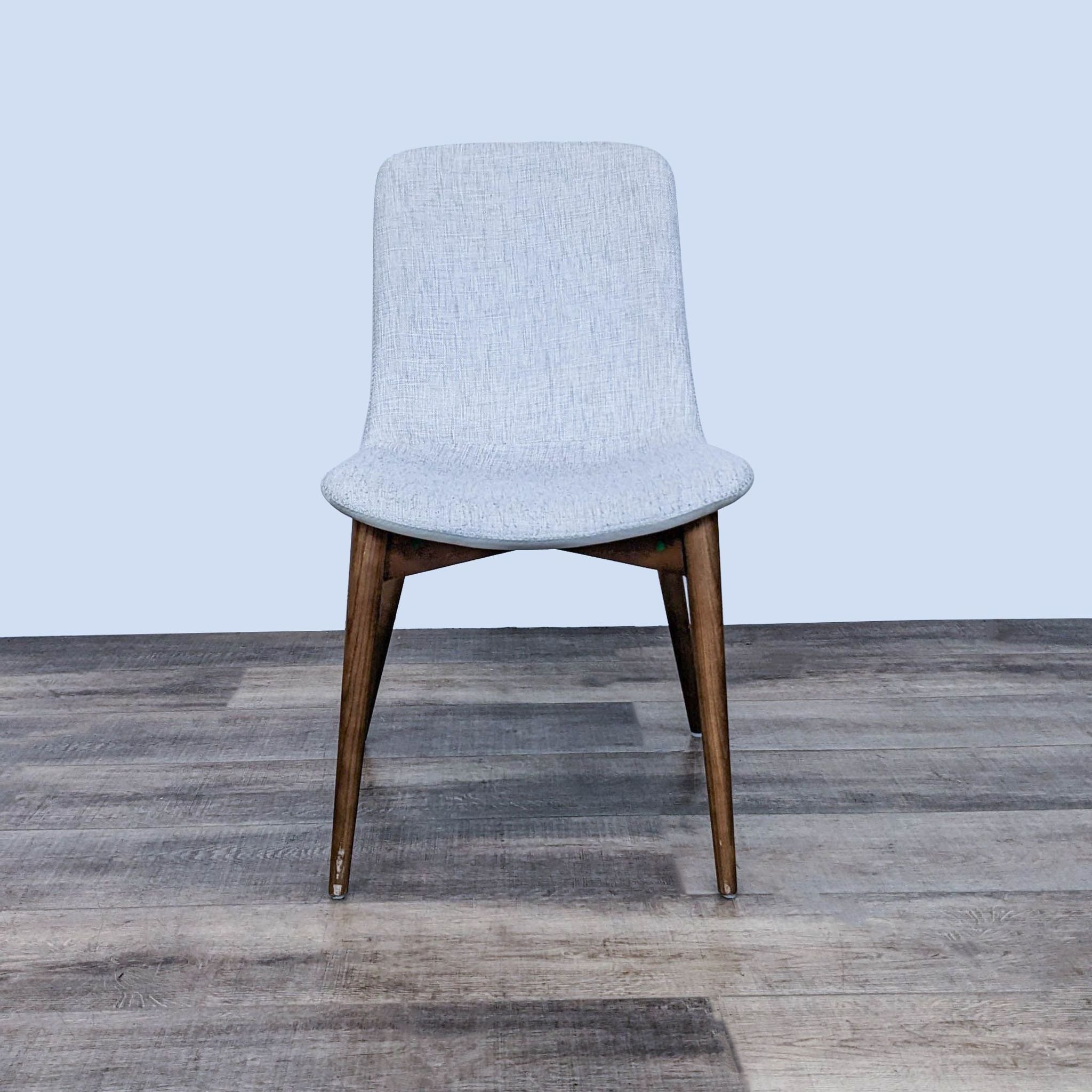 Reperch dining chair with a light fabric padded seat, detailed stitching, and wooden legs, in a natural setting.