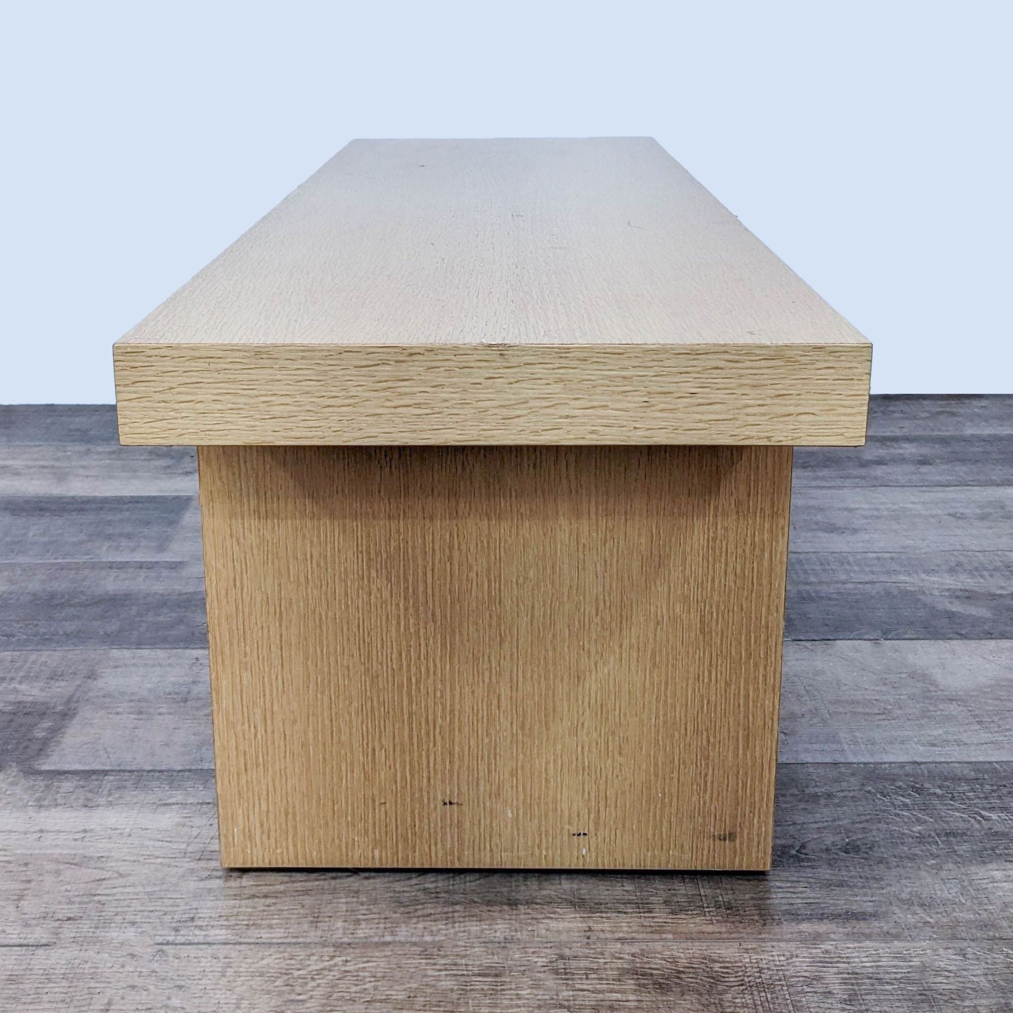 Reperch beech color modern bench with clean silhouette against a grey and wood floor background.
