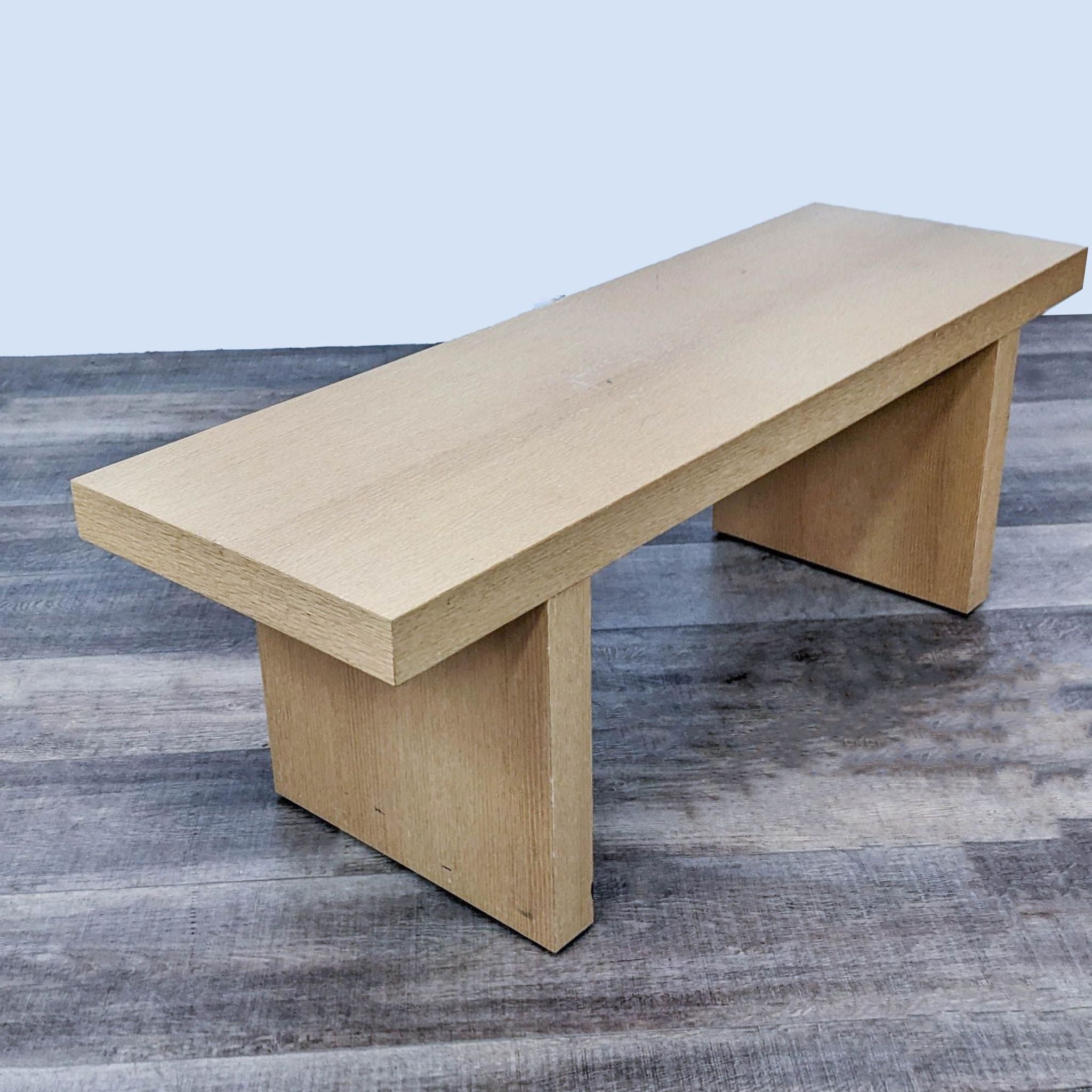 Sleek beech-colored Reperch bench showcasing modern design against a wooden floor, viewed from an angle.