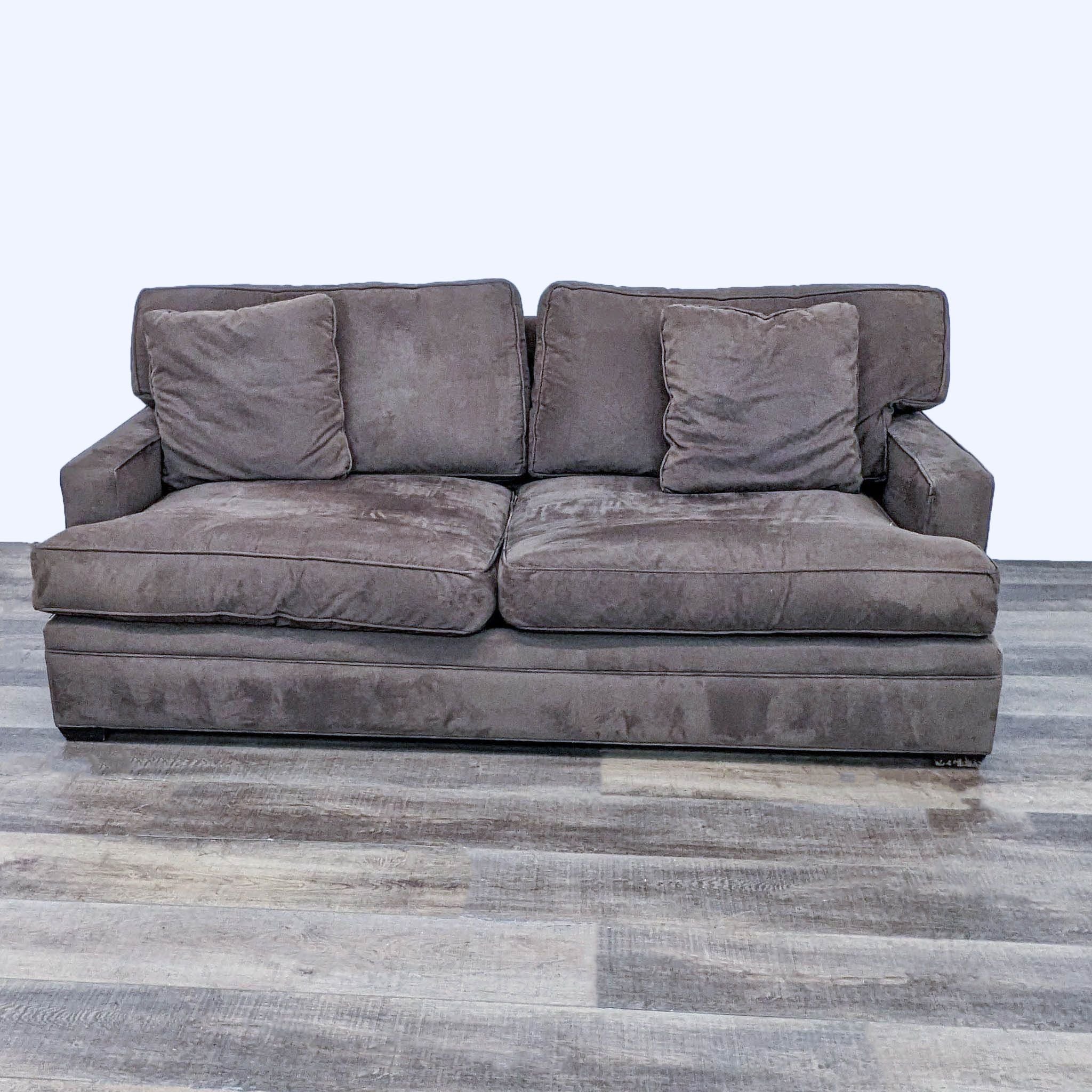 Crate & Barrel brown sleeper sofa with plush cushions and narrow arms, set on a wood-look floor.