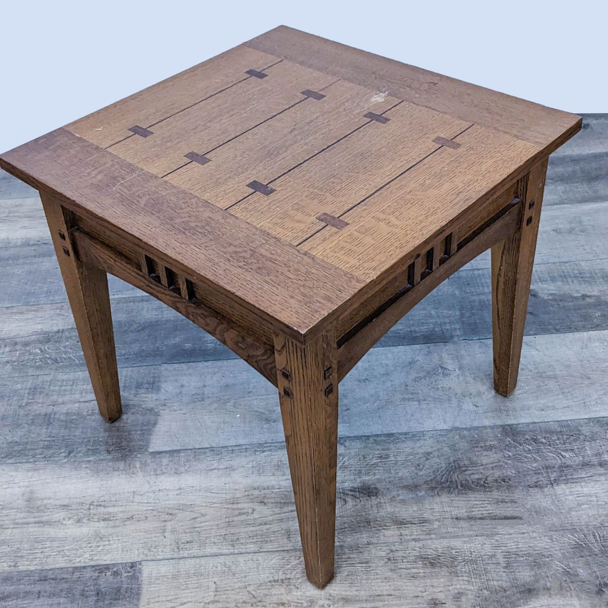 Reperch oak end table with decorative inlay on top and cut-out patterns on sides, on a grey wooden floor.